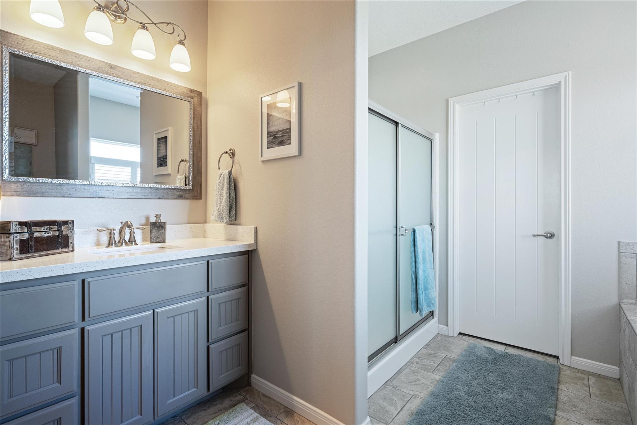 Bathroom with blue-gray vanity, framed mirror, and sliding glass shower enclosure.
