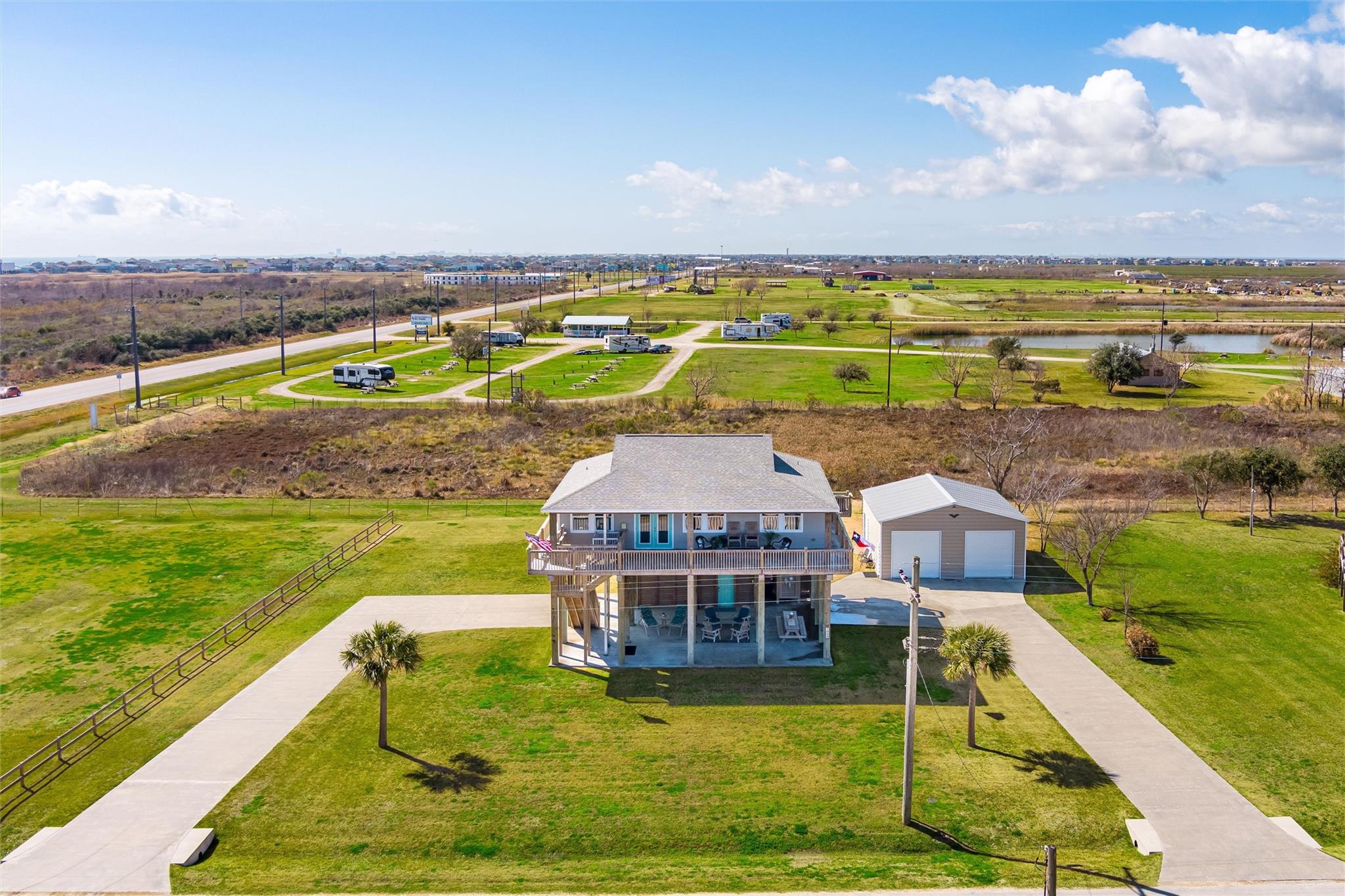 Aerial view of a raised home with a covered porch, detached garage, and expansive lawn.