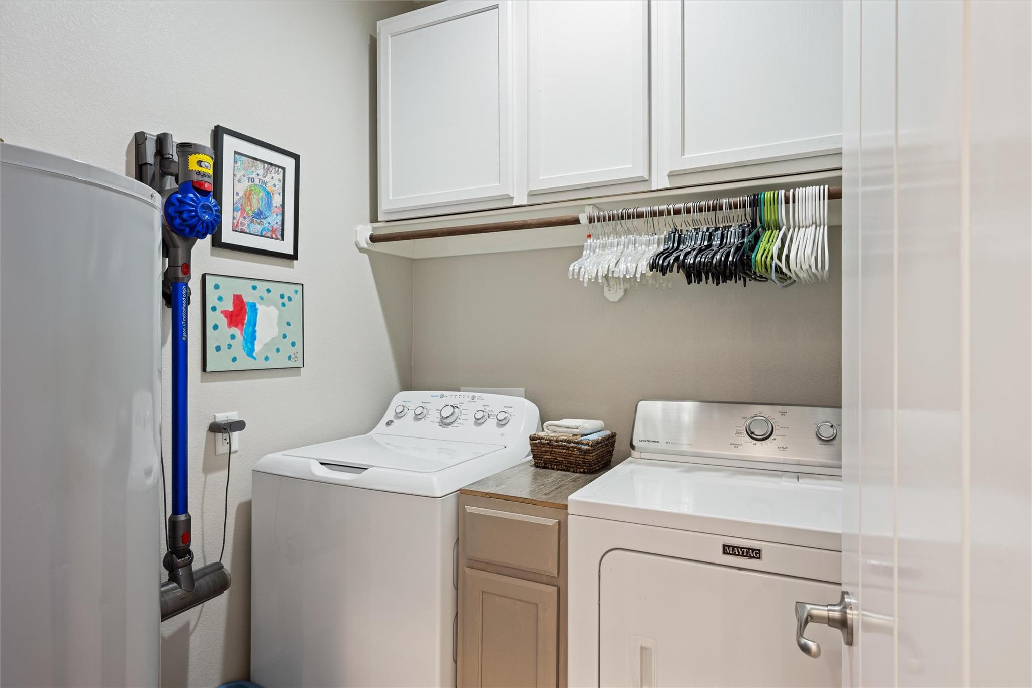 Laundry room with washer, dryer, overhead cabinets, and a rail of hangers.