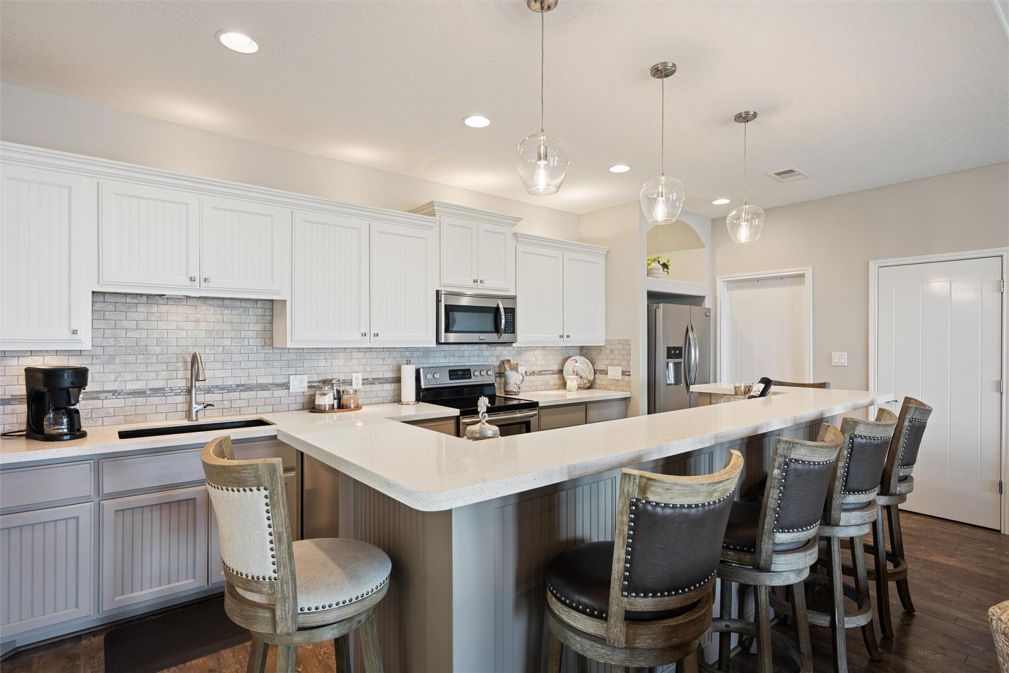 Kitchen with white cabinets, stainless steel appliances, and a large breakfast bar with upholstered stools.