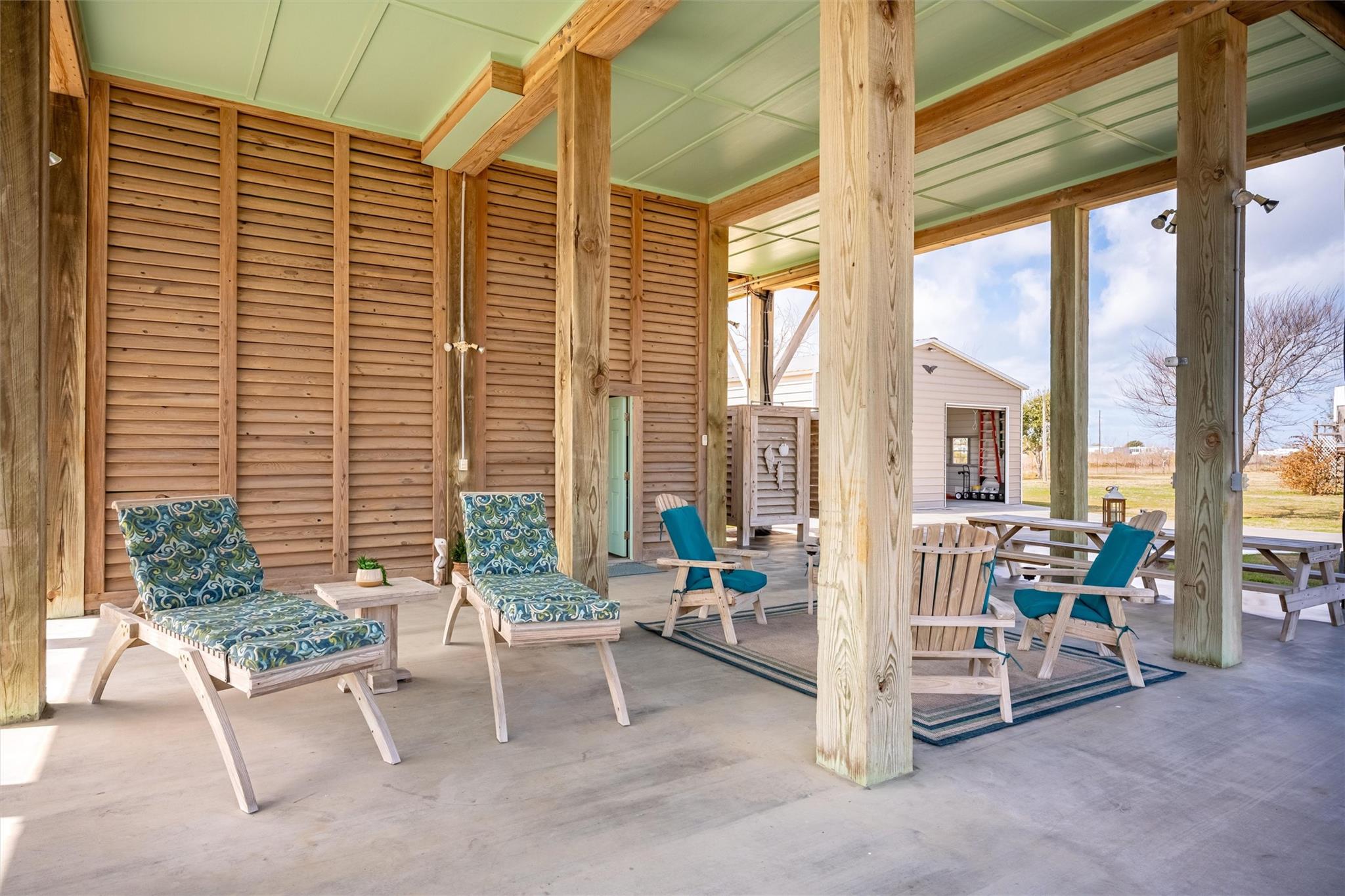 Covered wood patio with cushioned lounge chairs, Adirondack chairs, and picnic tables.