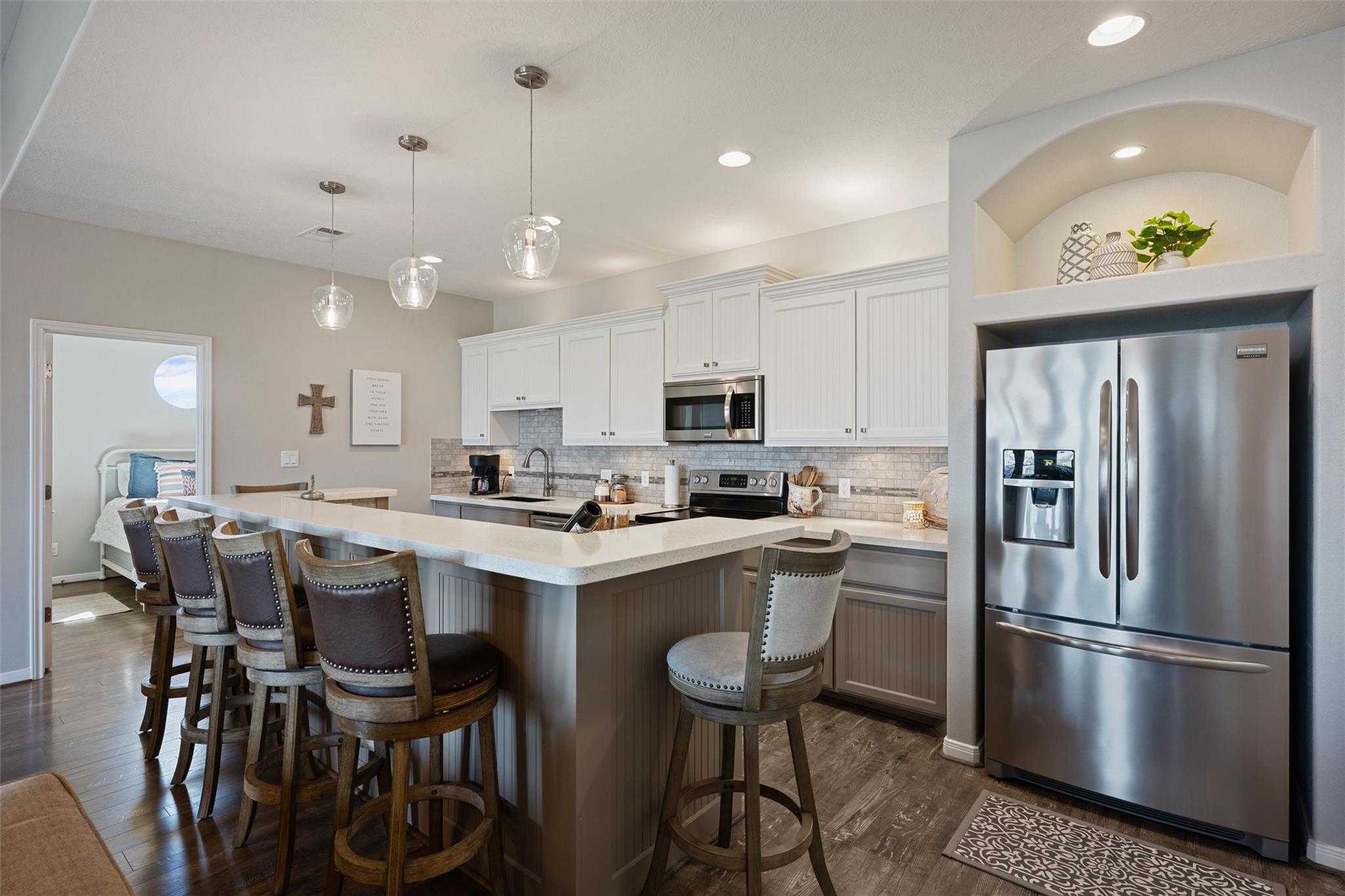 Kitchen with a large breakfast island, white cabinetry, pendant lights, and stainless steel appliances.