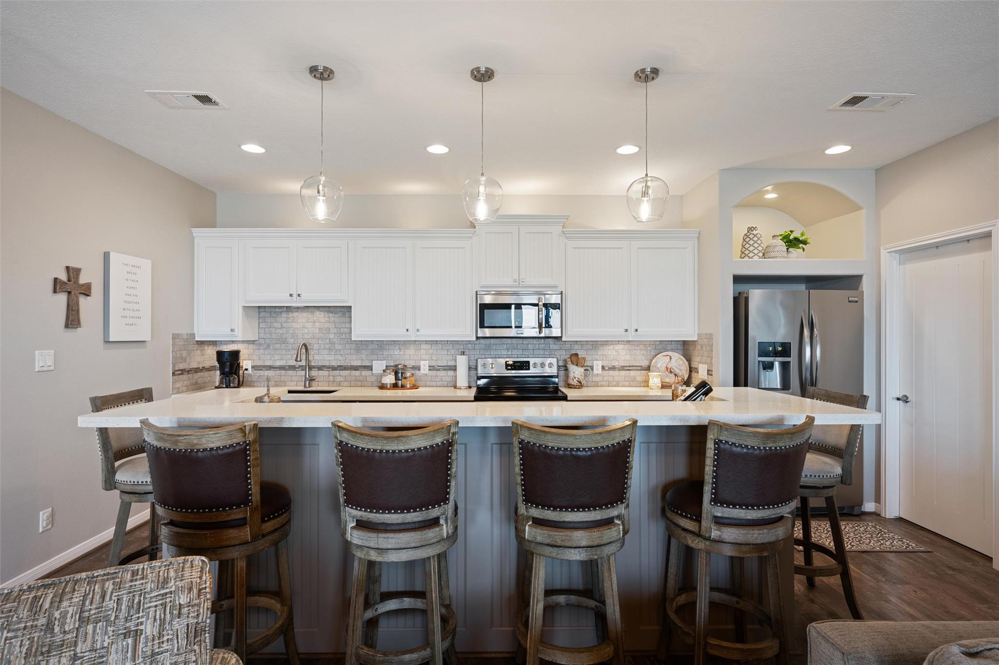 Kitchen with a large gray island, four bar stools, white cabinetry, and stainless steel appliances.