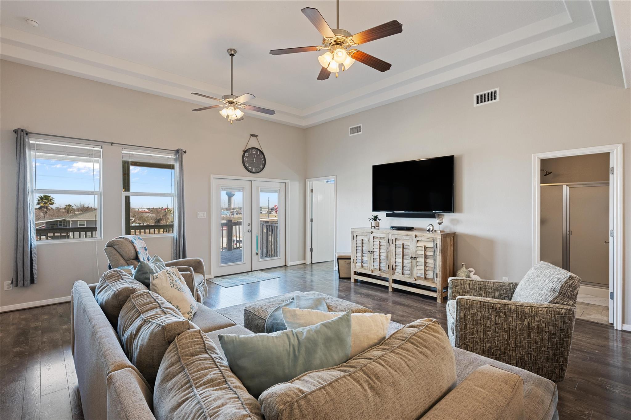 Furnished living room with two ceiling fans, glass deck doors, and a wall-mounted television.