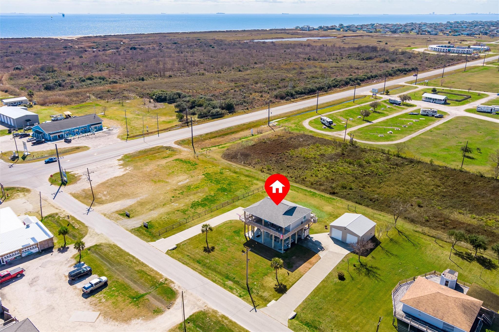 Elevated coastal home and detached garage, with open water visible beyond the surrounding roads and grassy lots.