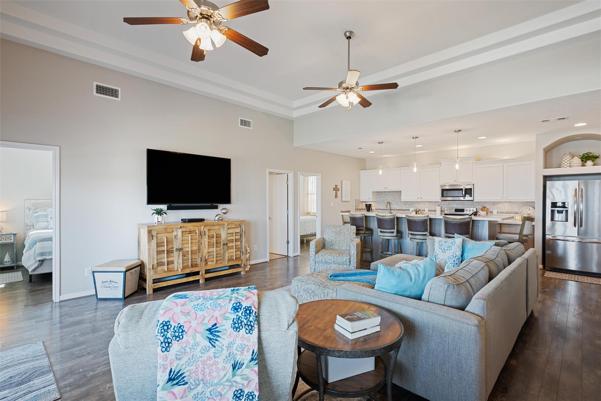 Open living room and kitchen with gray sofas, a wall-mounted television, and white cabinetry.