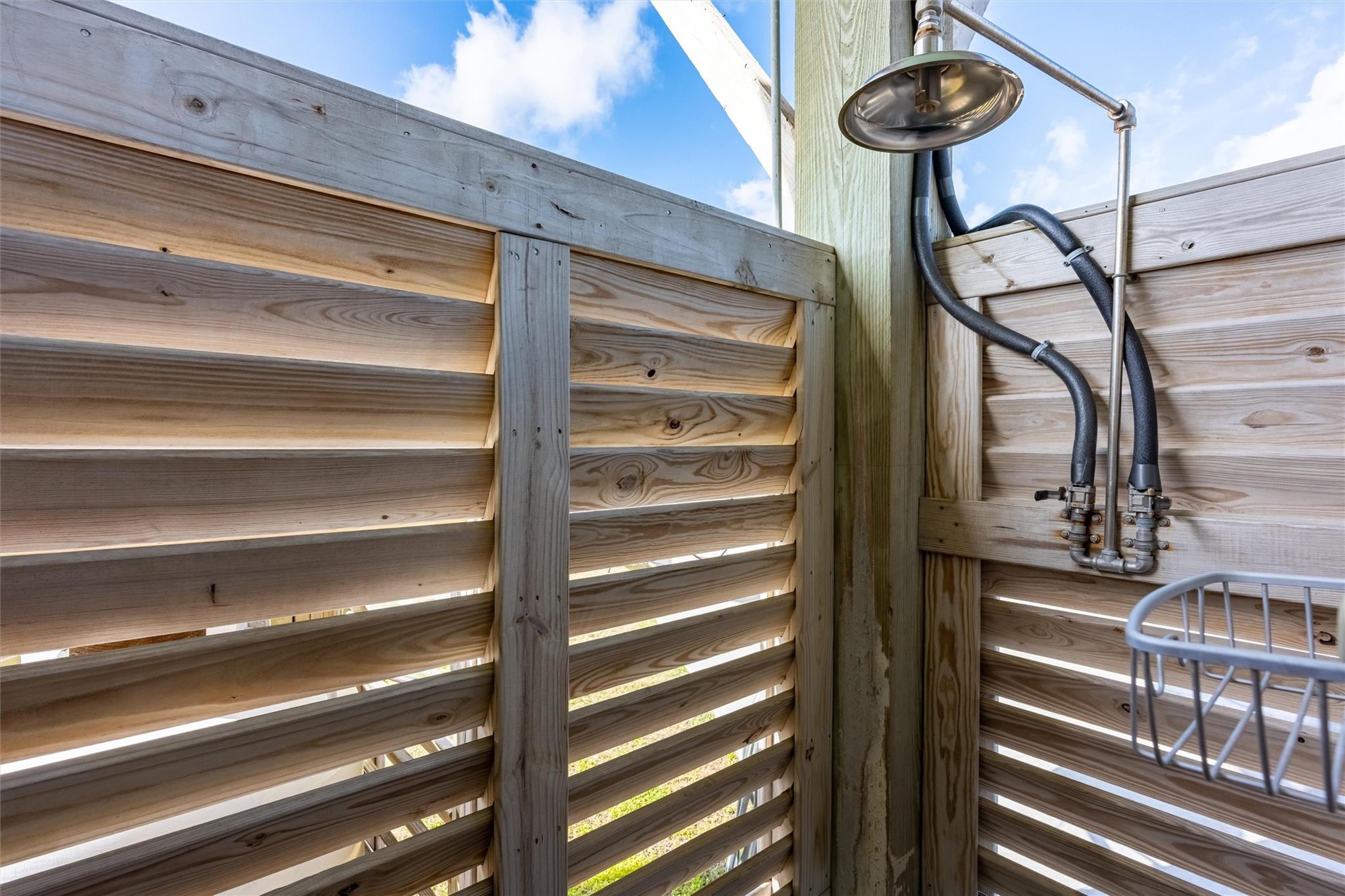 Outdoor shower with a metal showerhead and plumbing inside a wooden privacy enclosure.