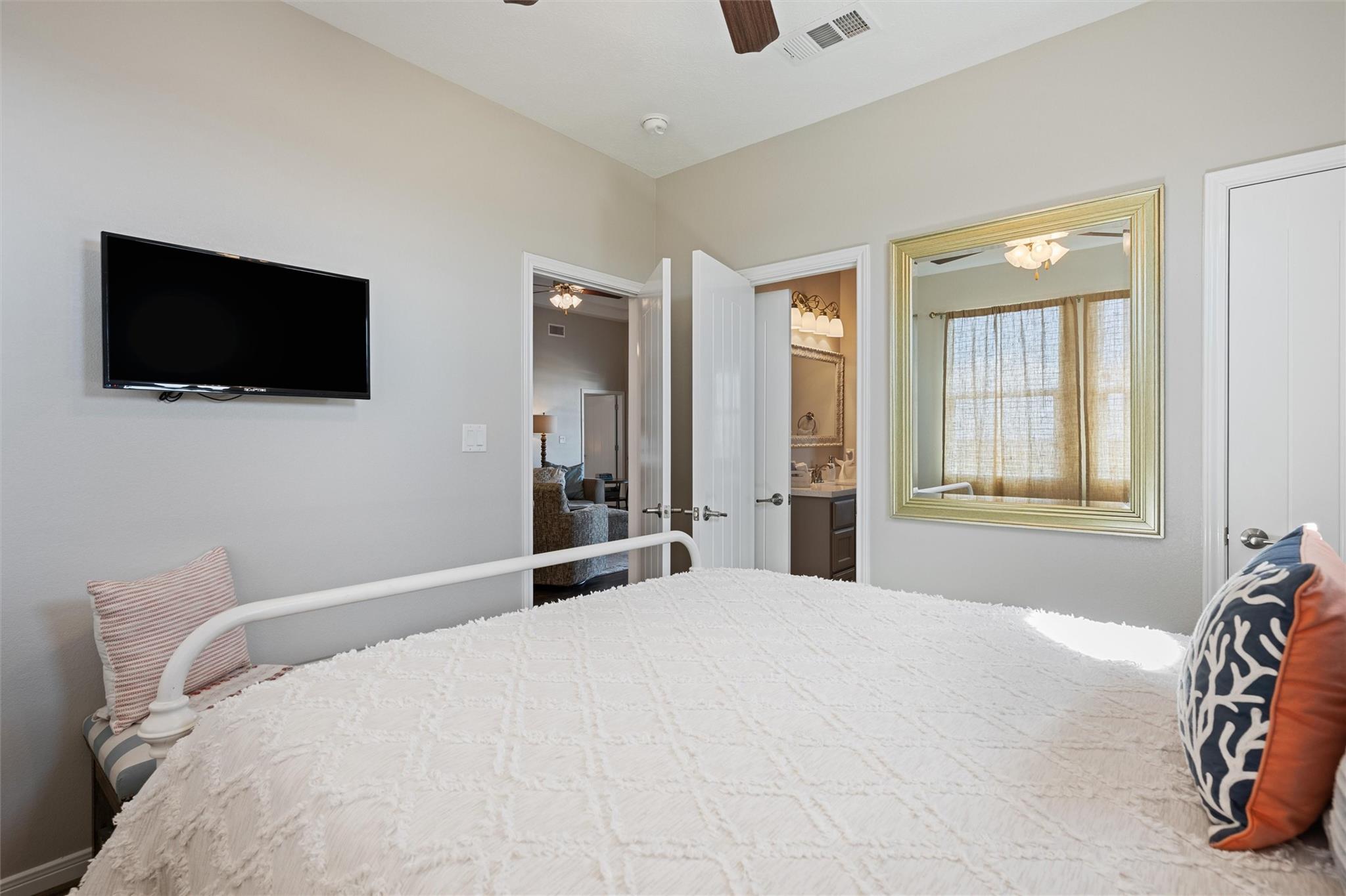 Bedroom with a white quilted bed, wall-mounted television, and large framed mirror.