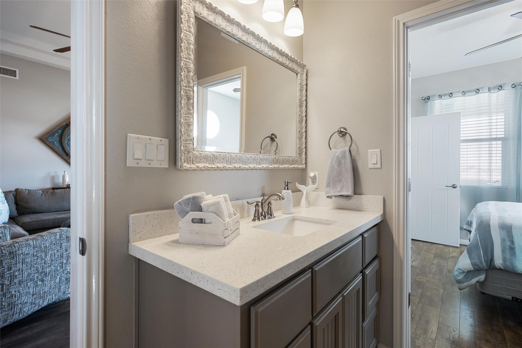 Bathroom vanity with a speckled countertop and ornate mirror, opening onto a bedroom.