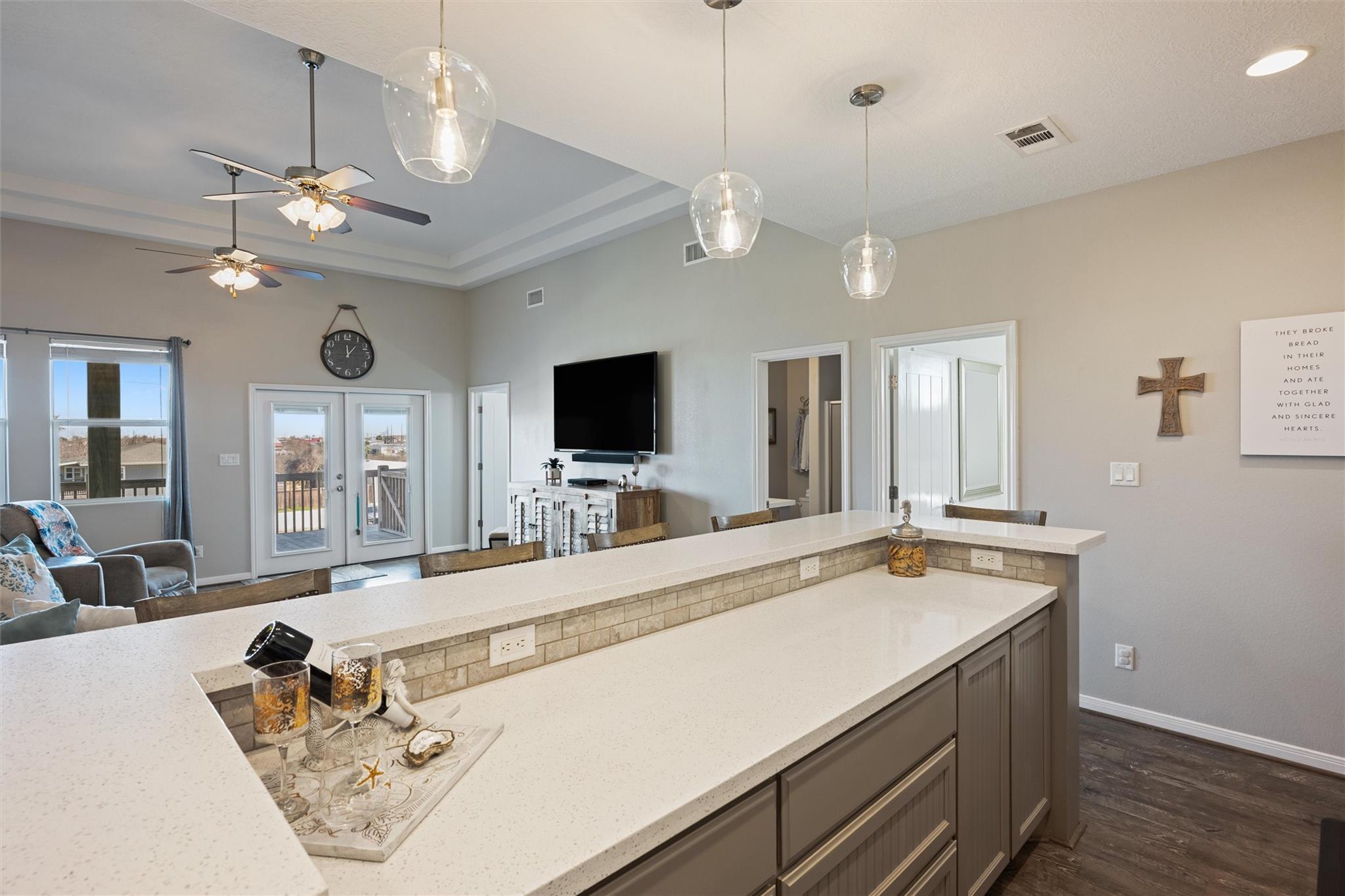 Open-plan kitchen with a long white island overlooking a living area with French doors to a deck.