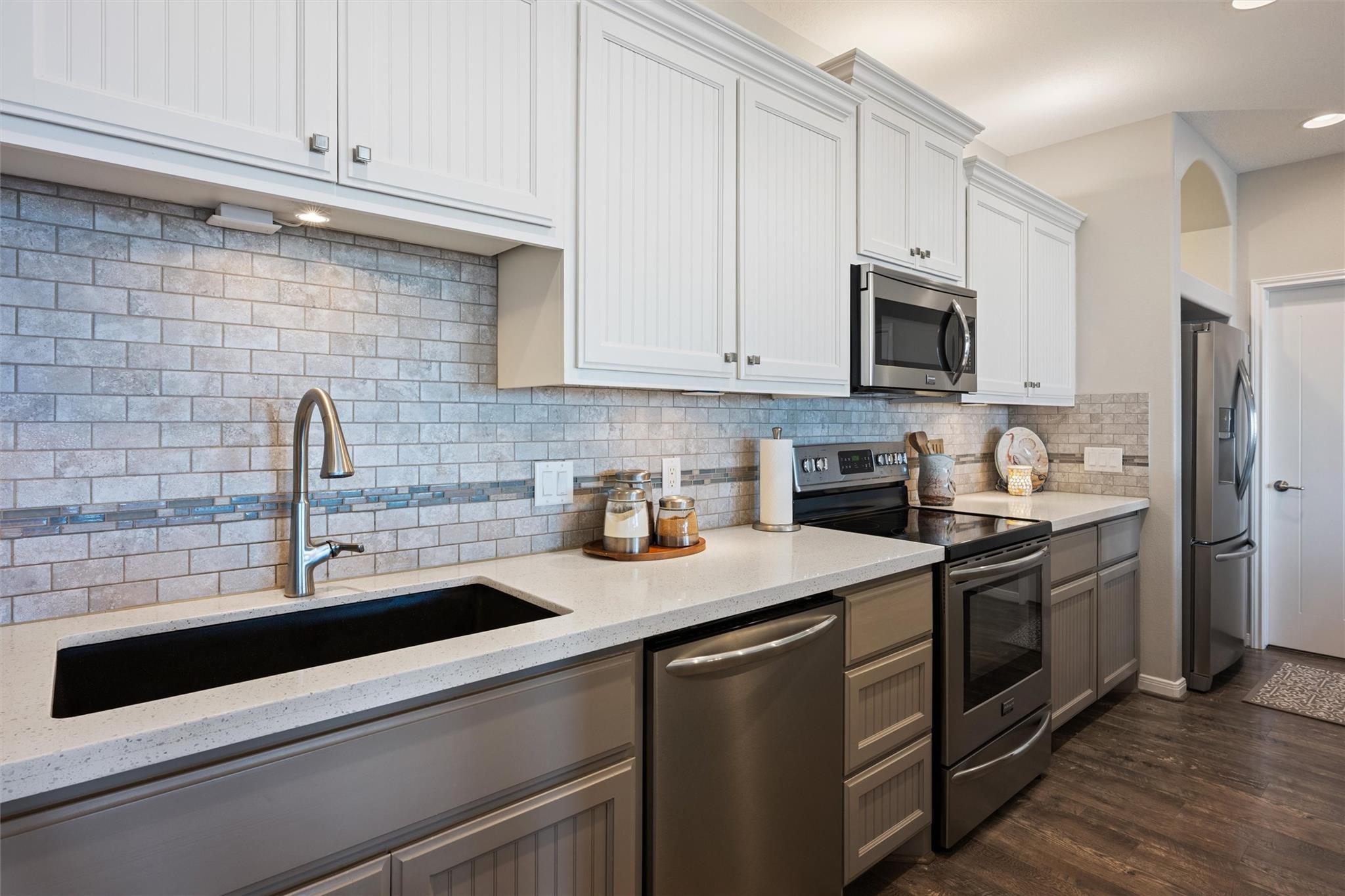 Kitchen with white cabinets, gray tile backsplash, black sink, and stainless steel appliances.