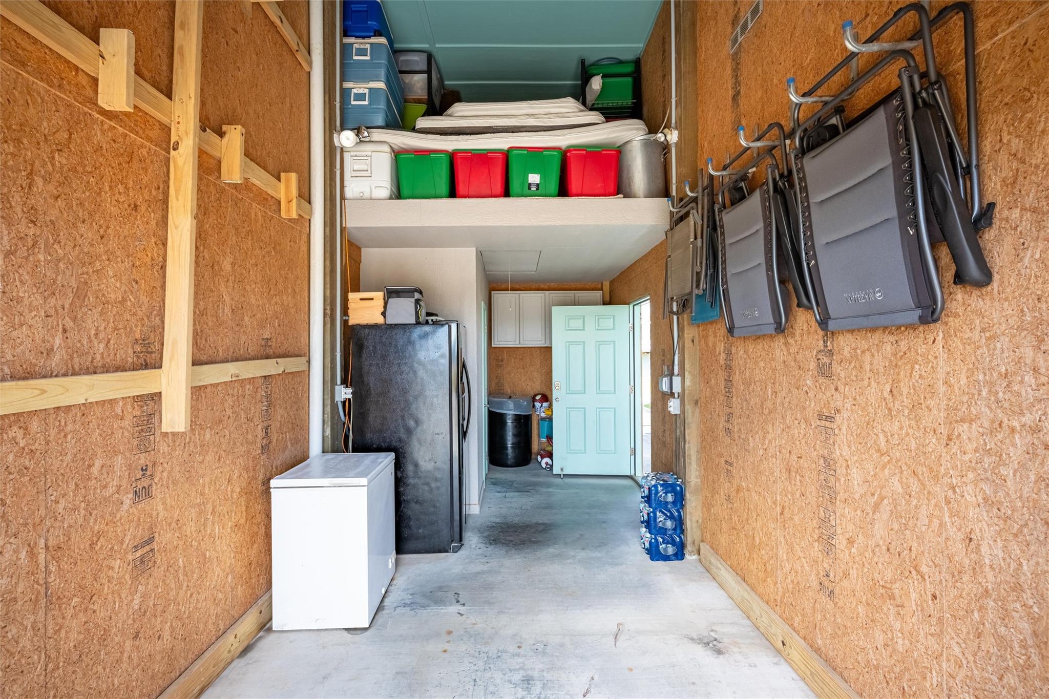 Garage with overhead storage, wall-mounted folding chairs, a chest freezer, and refrigerator.