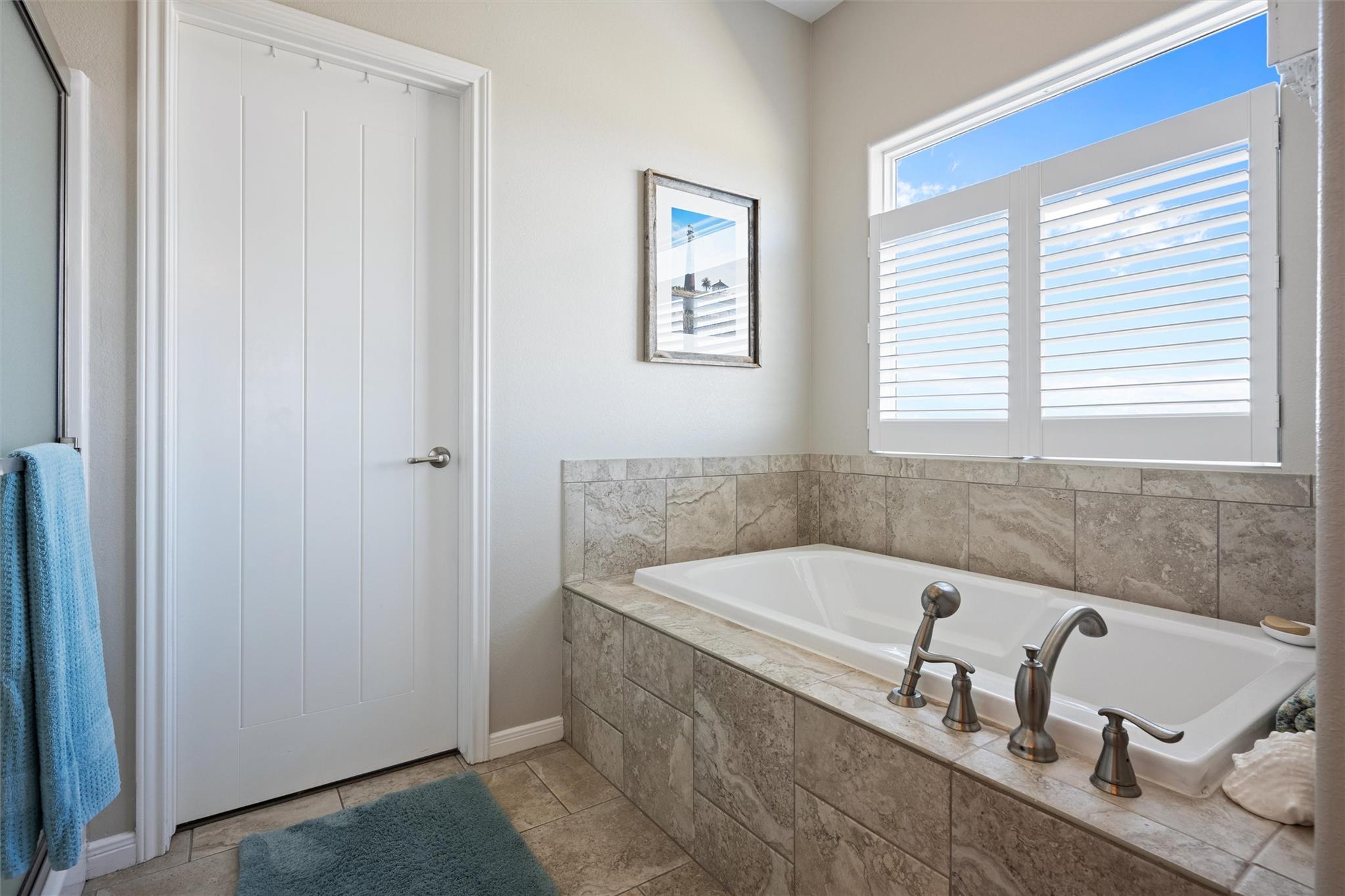 Bathroom with a tiled soaking tub and plantation shutters over a bright window.