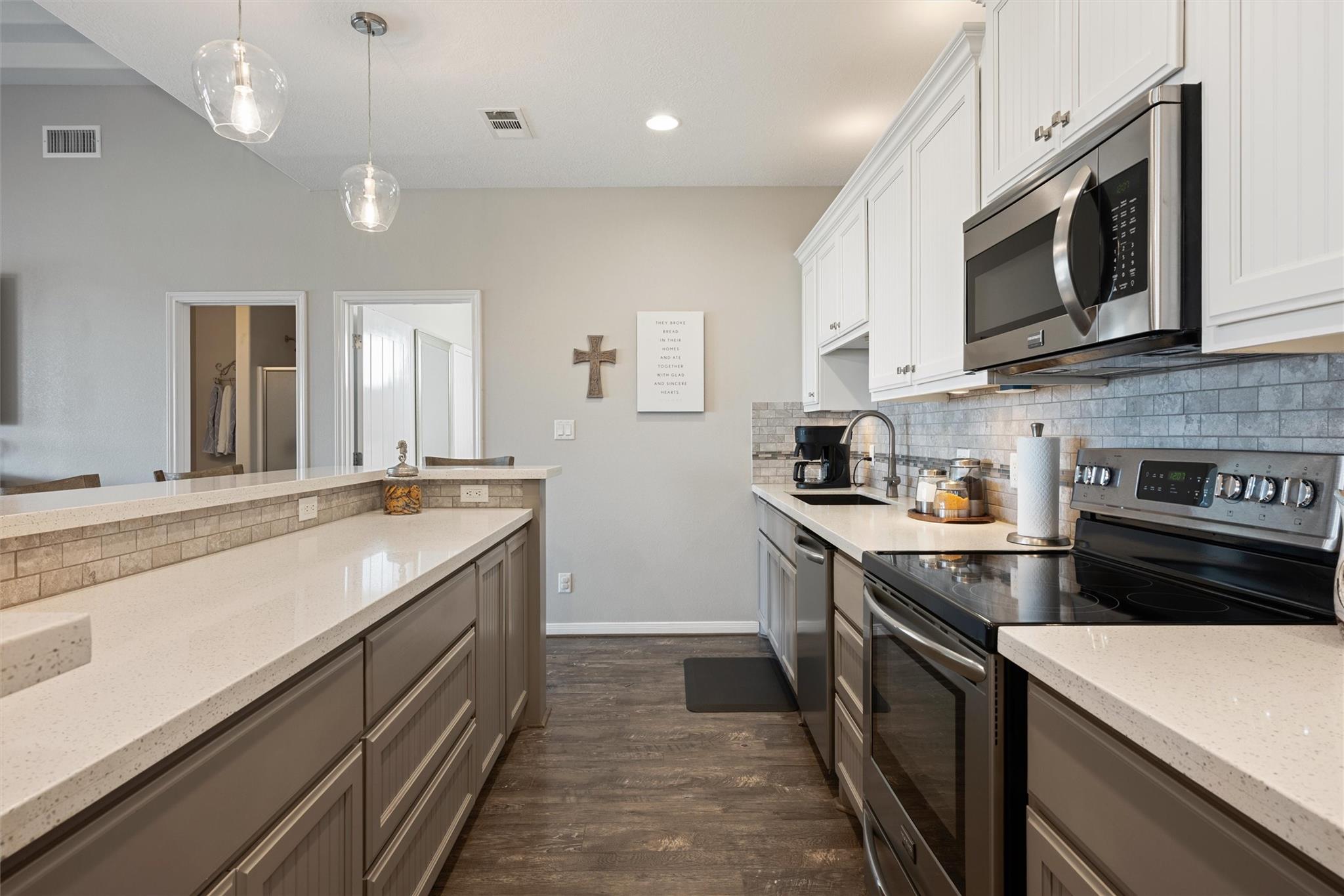 Kitchen with a stone-topped island, white cabinets, gray tile backsplash, and stainless steel appliances.