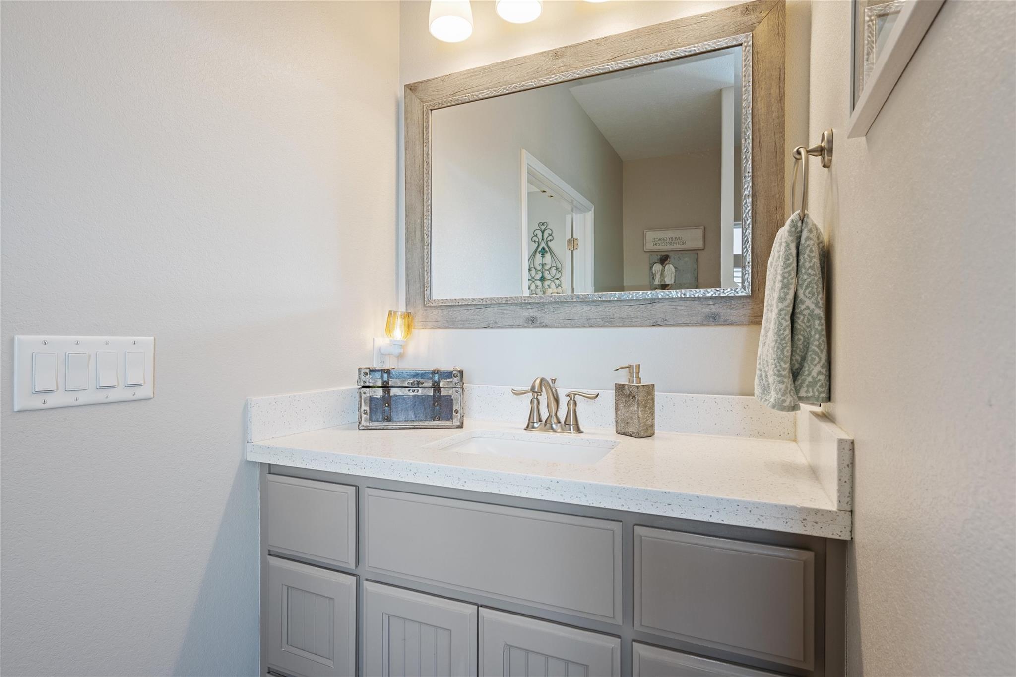 Bathroom vanity with gray paneled cabinets, a white countertop, and a large framed mirror.