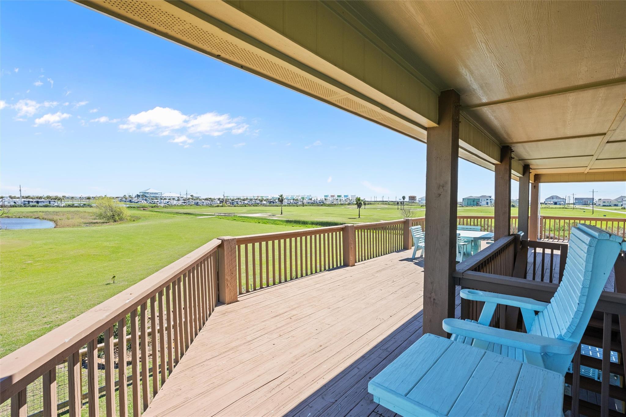 Covered wooden deck with blue Adirondack chairs overlooking a lawn and pond.