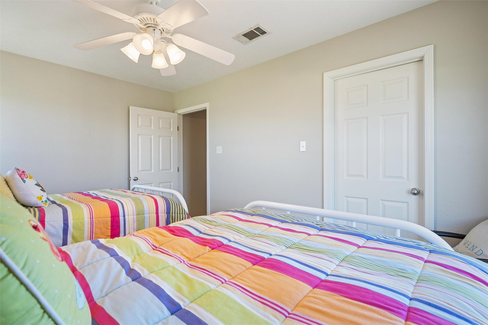 Bedroom with two beds dressed in colorful striped patchwork quilts and a white ceiling fan.