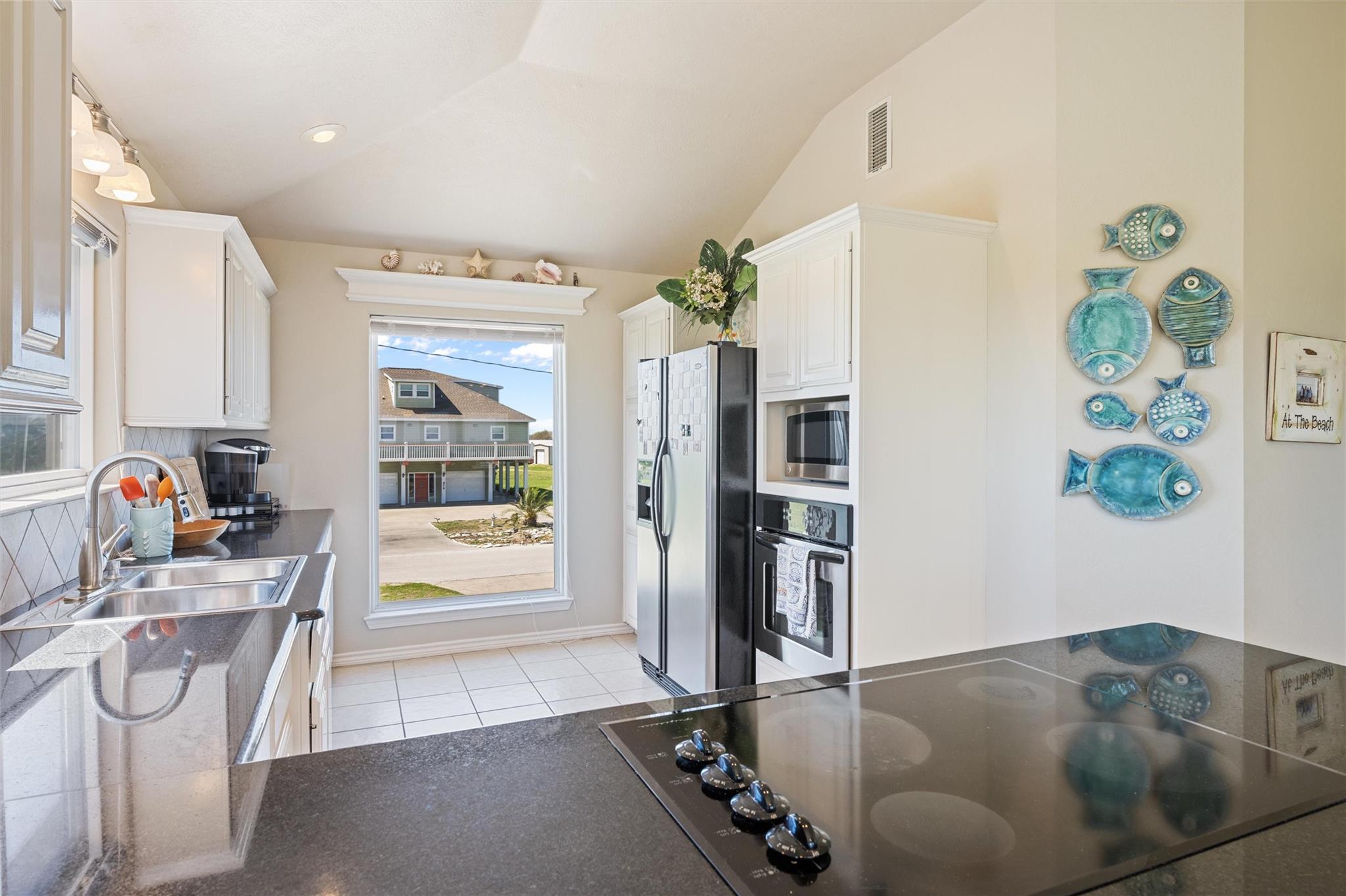 Bright kitchen with white cabinetry, stainless appliances, and blue fish wall decorations.