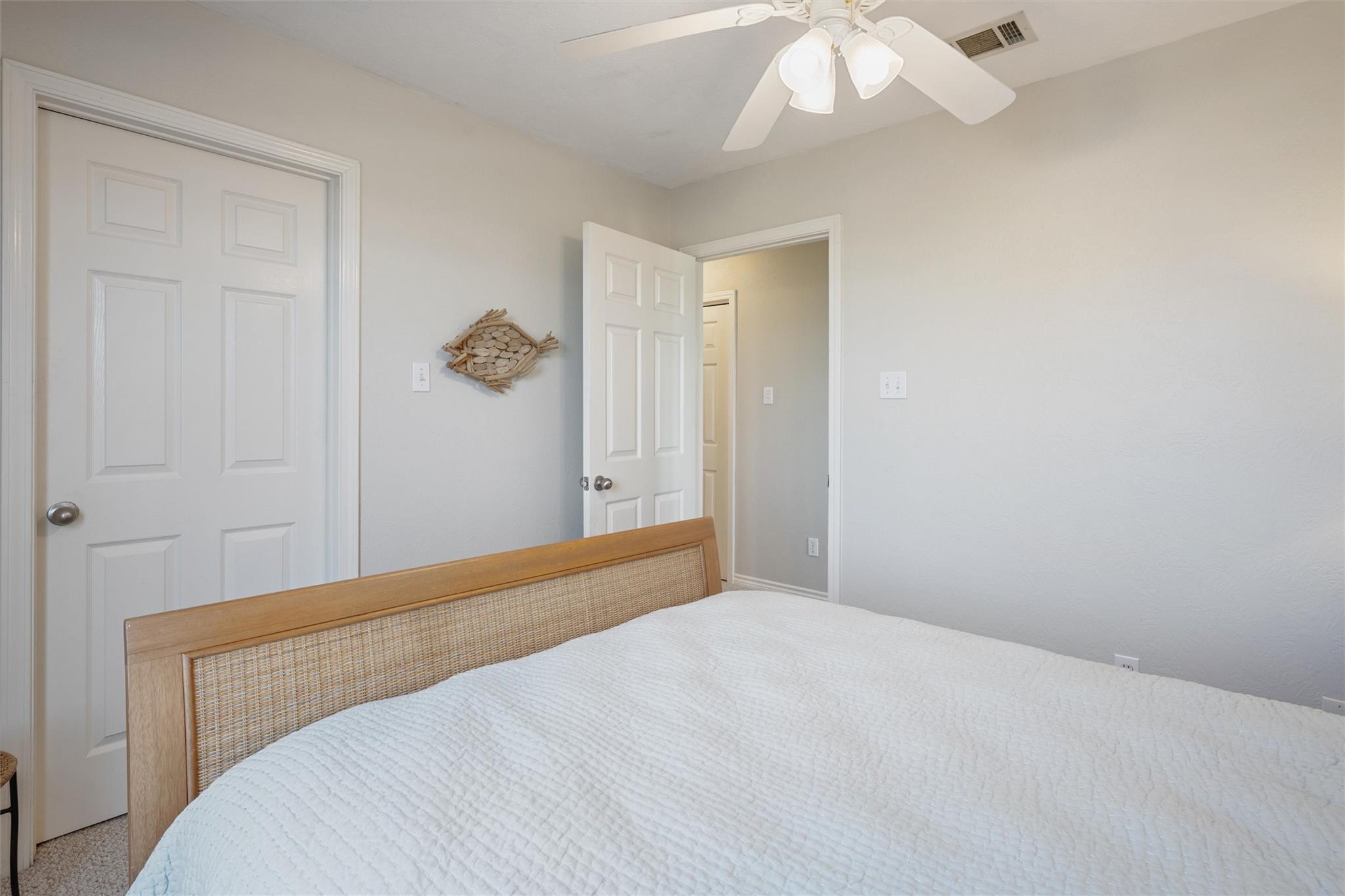 Bedroom with a white quilted bed, woven cane headboard, ceiling fan, and fish-shaped wall decor.