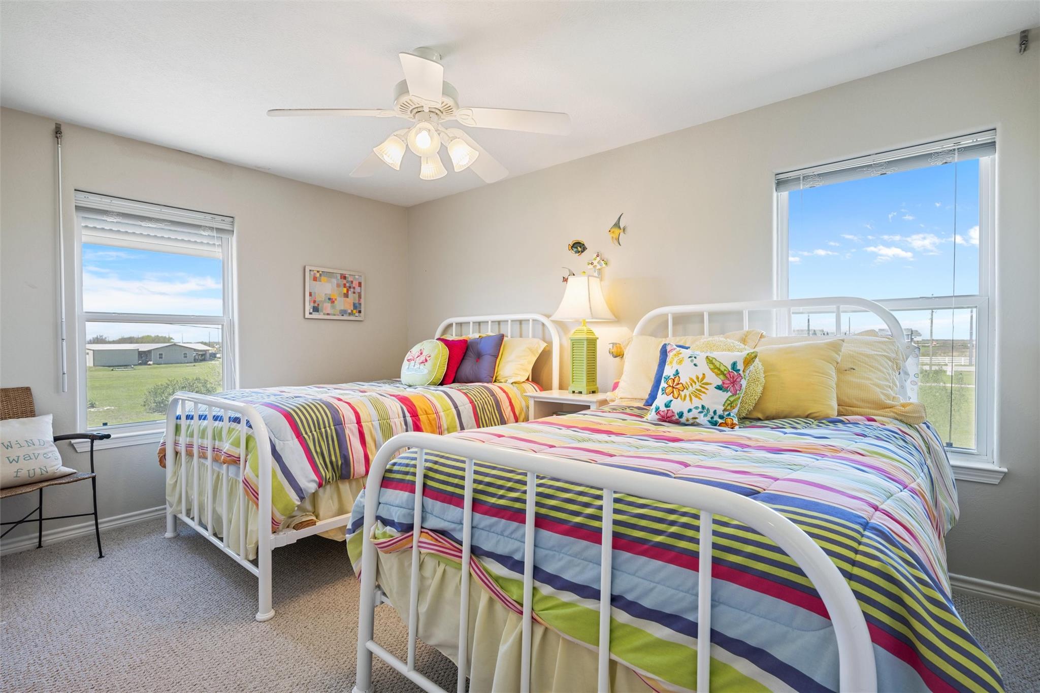 Bedroom with two white twin beds, colorful striped quilts, and large windows.