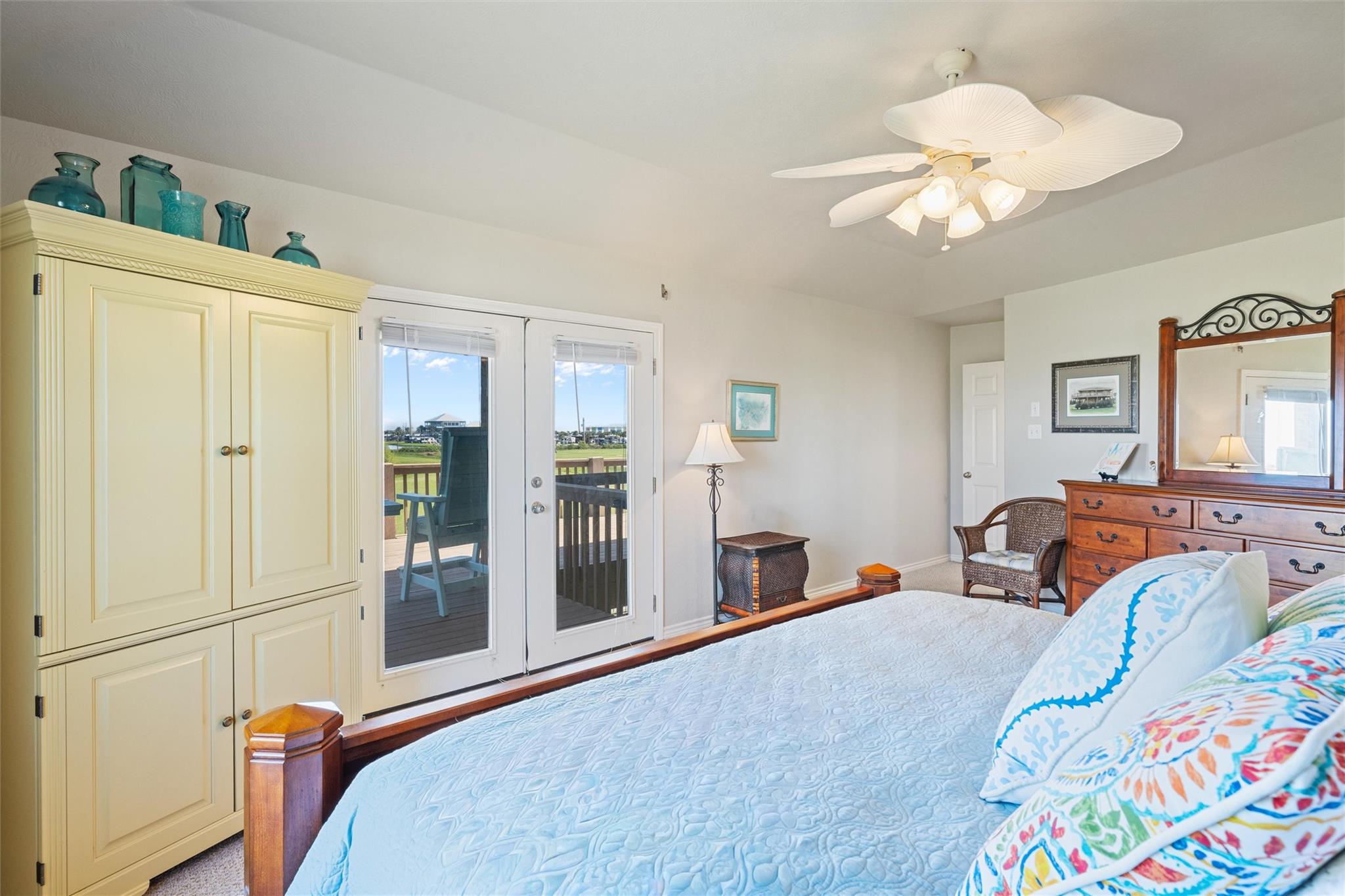 Furnished bedroom with a pale blue bedspread, cream armoire, and glass doors opening onto a deck.