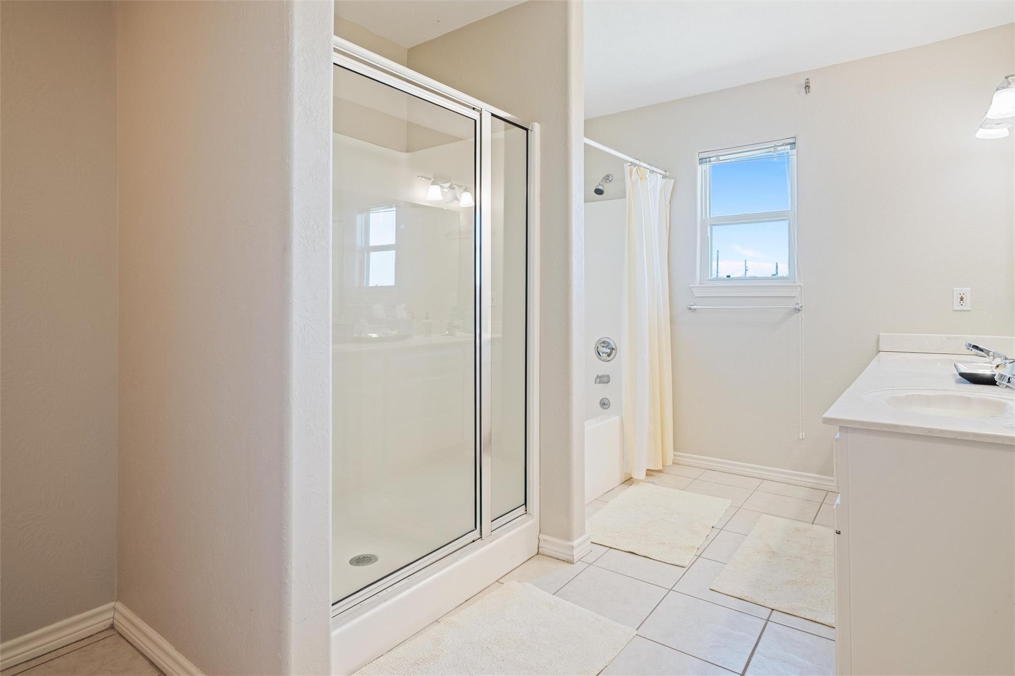 Bathroom with glass shower, separate tub, window, and white vanity.