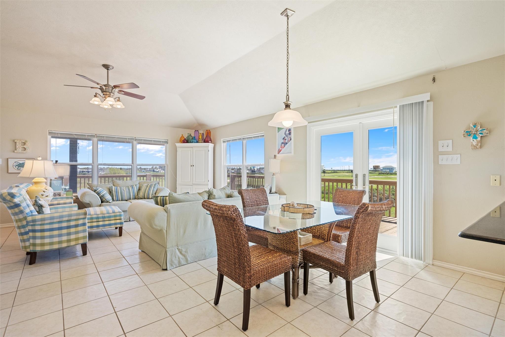 Open-plan living and dining room with vaulted ceiling, wicker dining chairs, and sliding doors to a deck.
