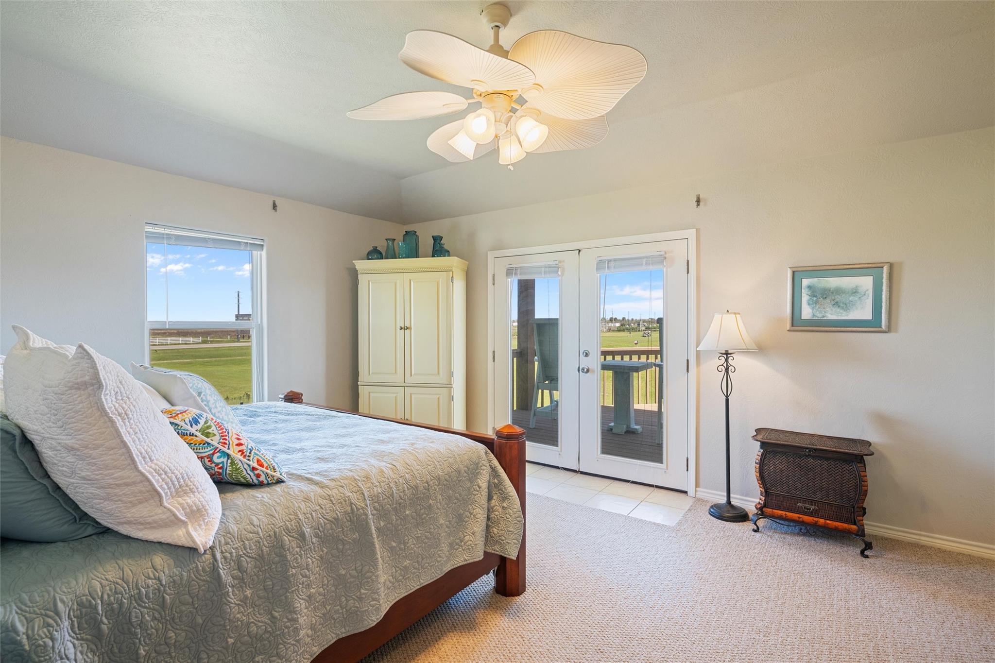 Bedroom with a quilt-covered bed and French doors opening onto a deck overlooking grass.