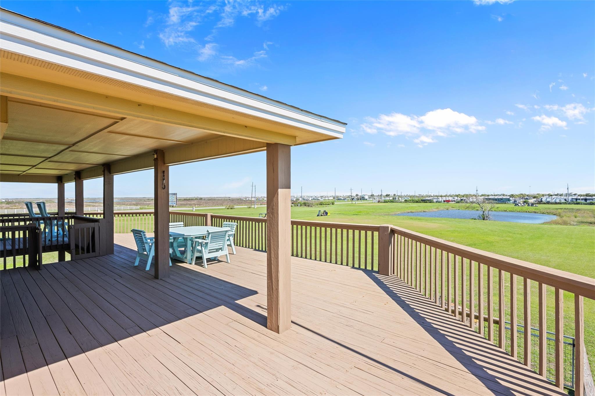 Covered wooden deck with outdoor dining furniture overlooking a green lawn and small pond.