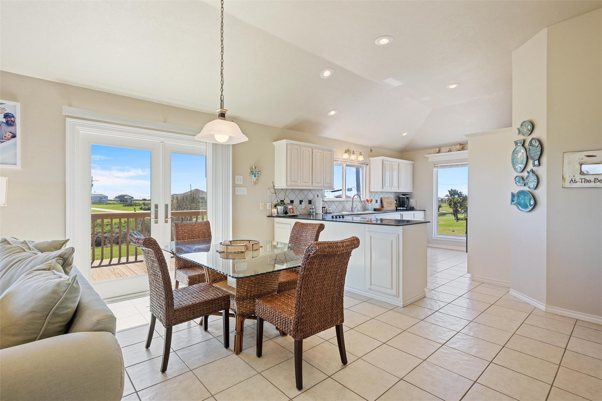Open-plan dining area and kitchen with wicker chairs, white cabinets, and sliding doors to a deck.