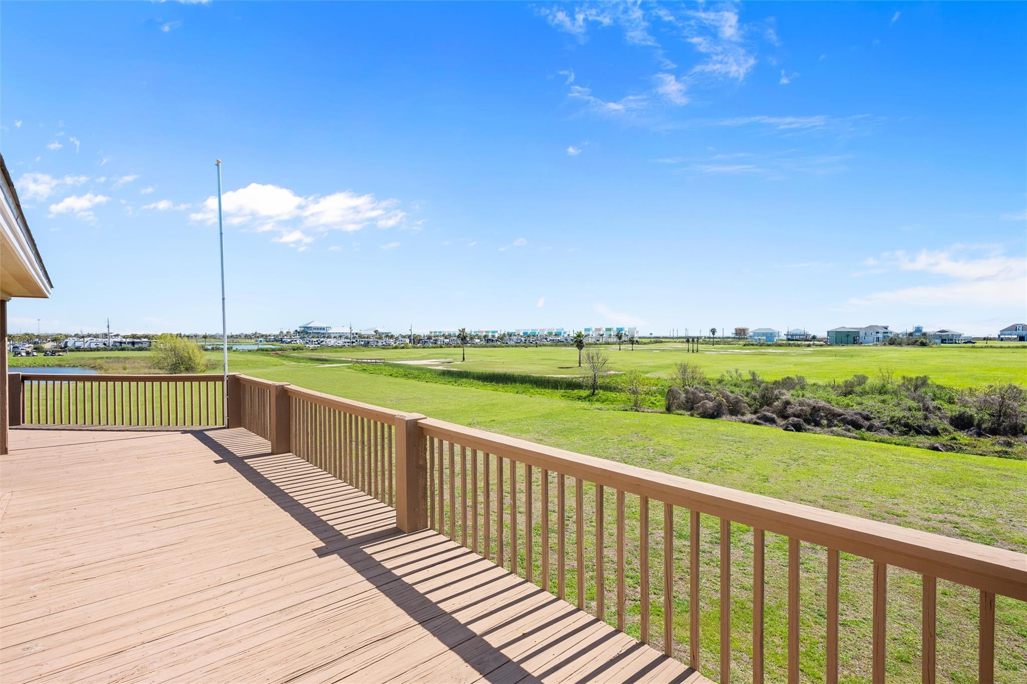 Wooden deck overlooking a broad green landscape and distant buildings.