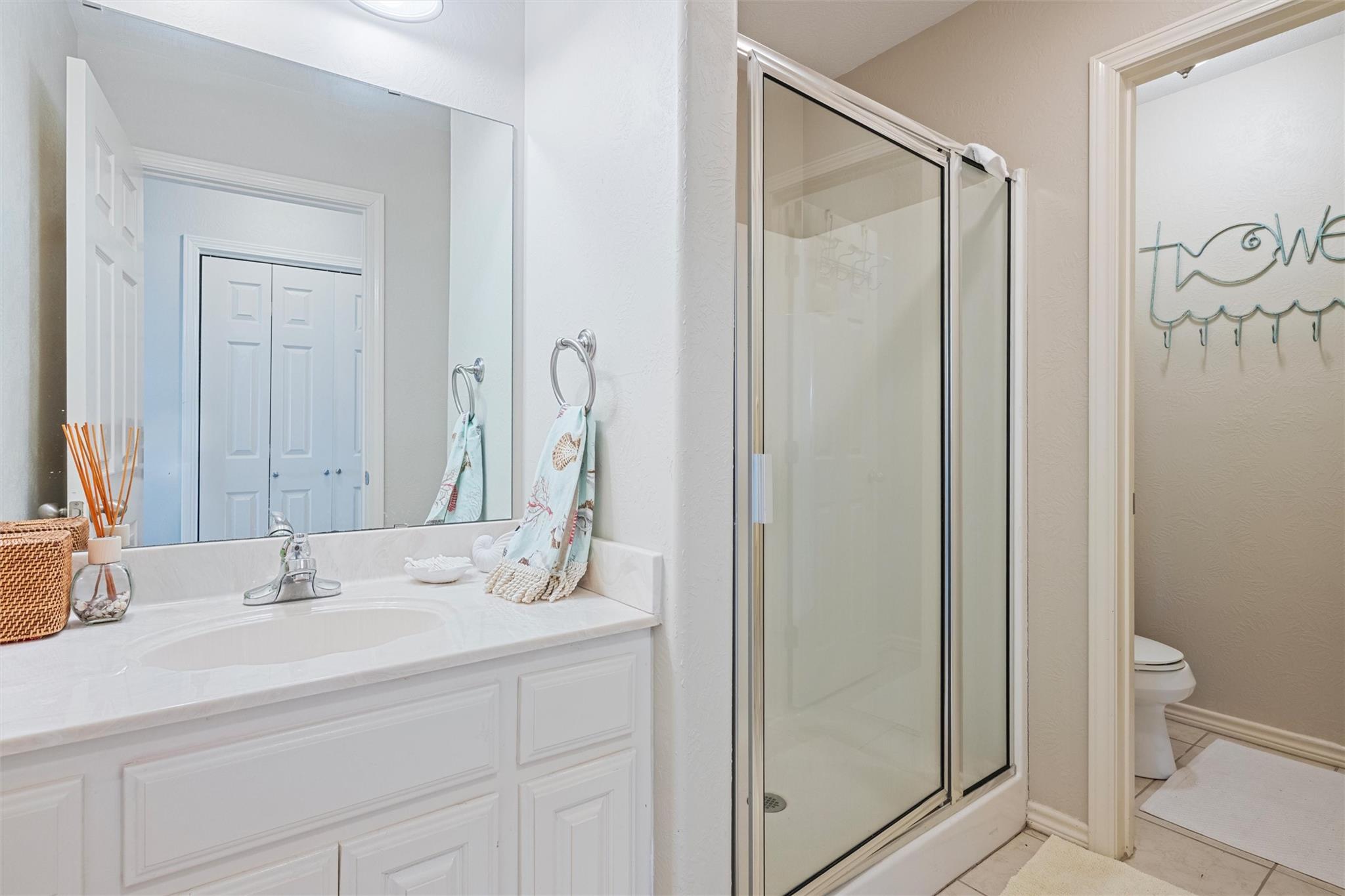 Bathroom with white vanity, glass shower enclosure, and a separate toilet area.