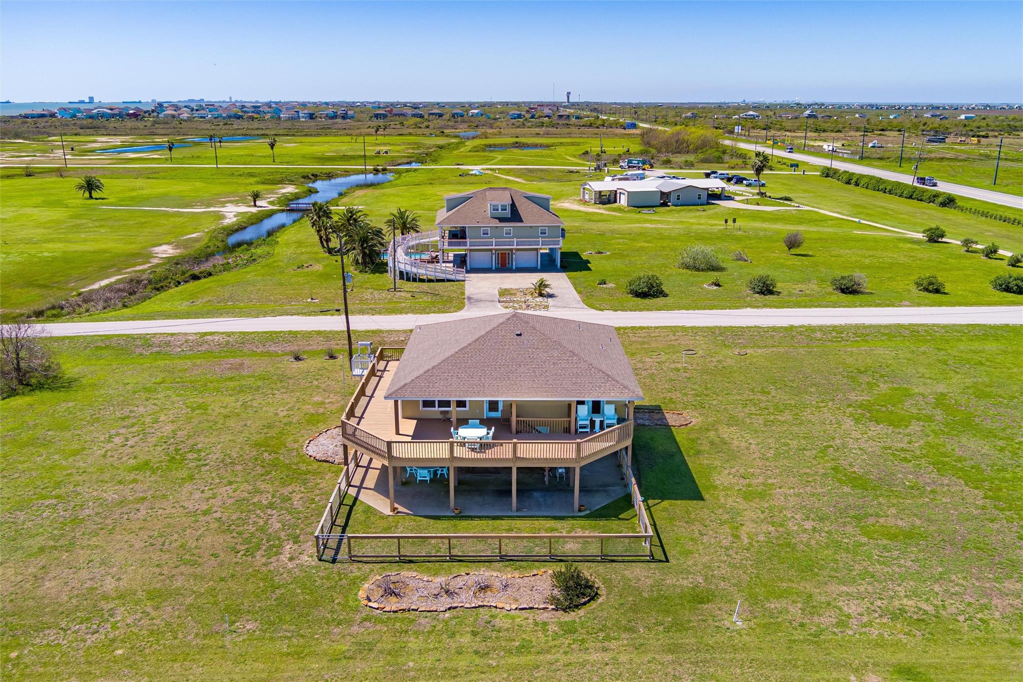 Raised coastal home with a wraparound deck on a broad grassy lot beside a marsh channel.