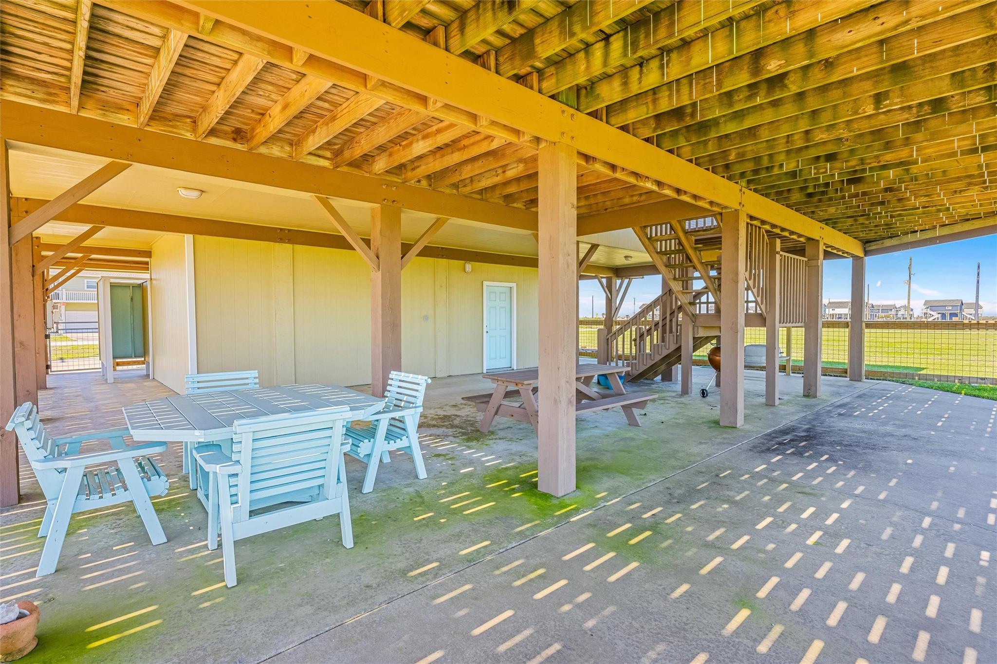 Covered patio beneath a raised home with white dining furniture and stairs to the upper level.