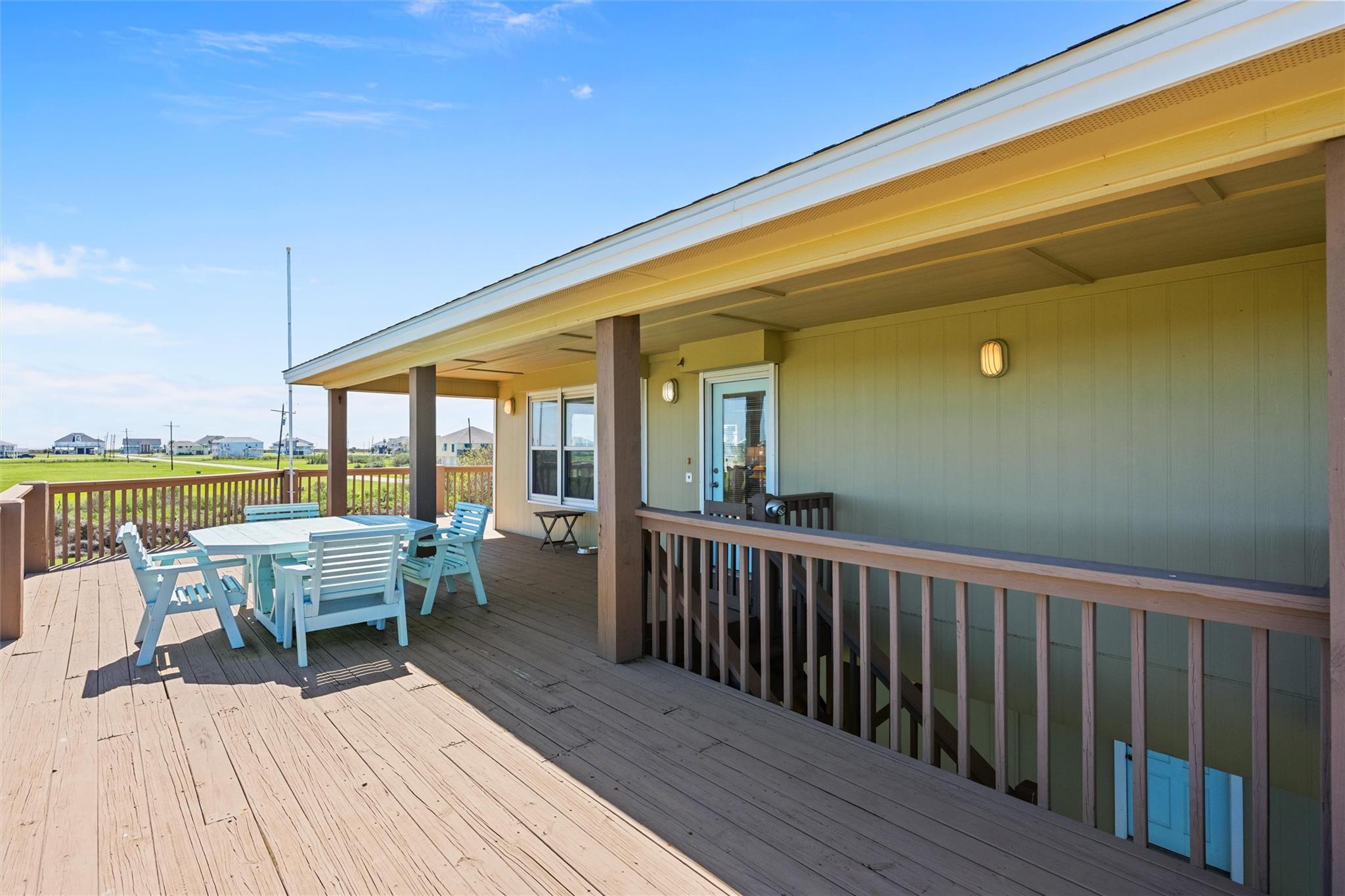 Covered wooden deck with pale blue dining furniture and views across grassy lots to nearby homes.