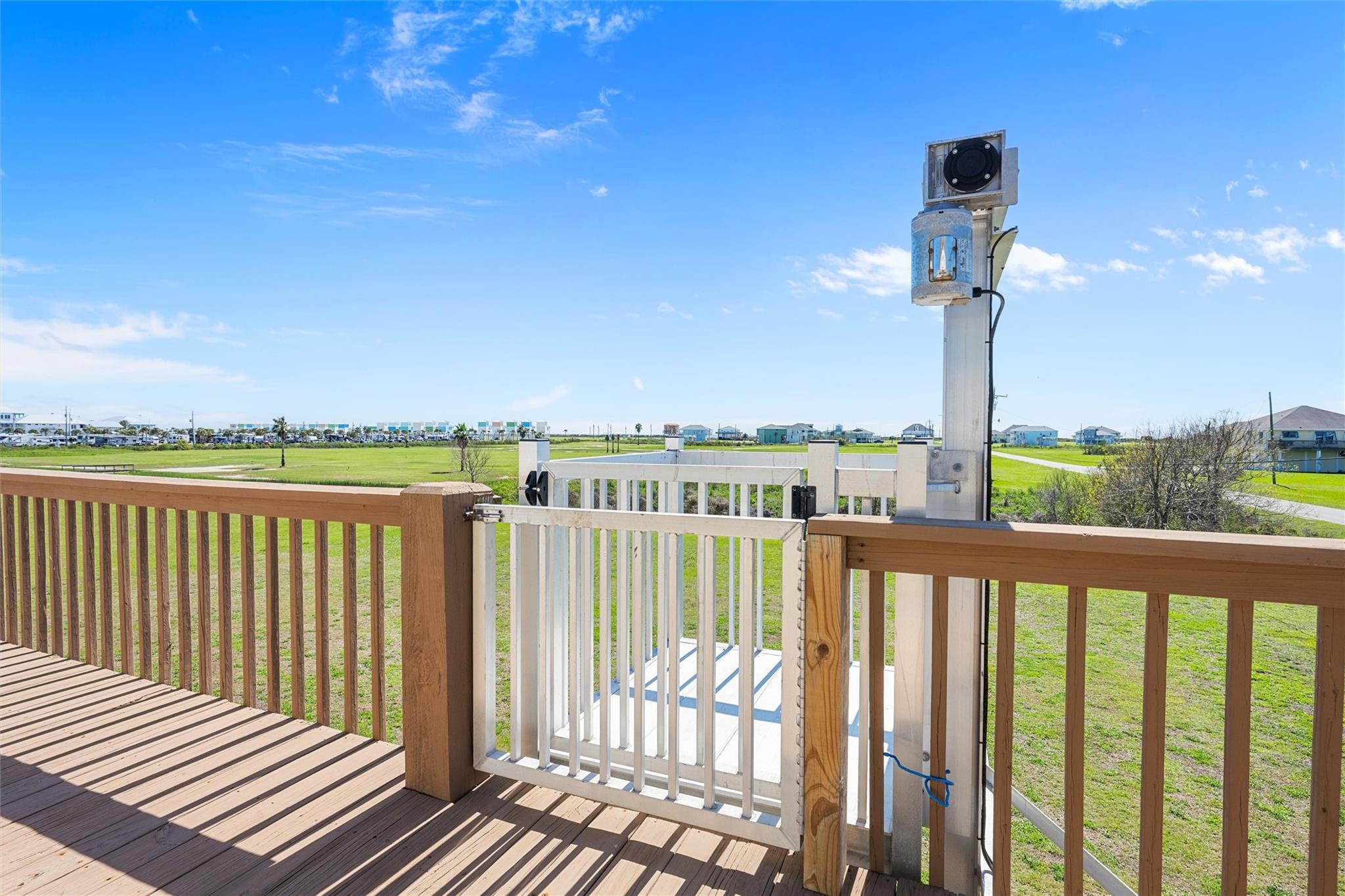 Wooden deck with a white platform lift overlooking a green lawn and distant homes.