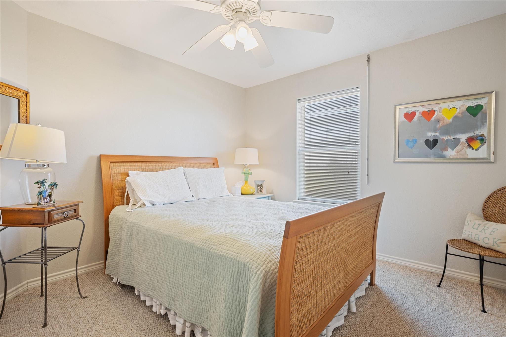 Bedroom with a wood-and-cane bed, white bedding, and framed colorful heart artwork.