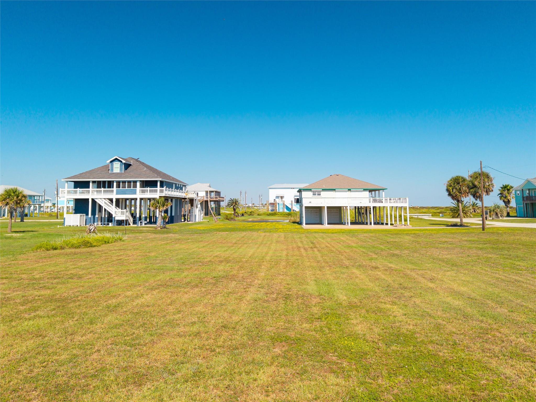 Elevated coastal homes with broad decks stand beyond a wide, sunny lawn.