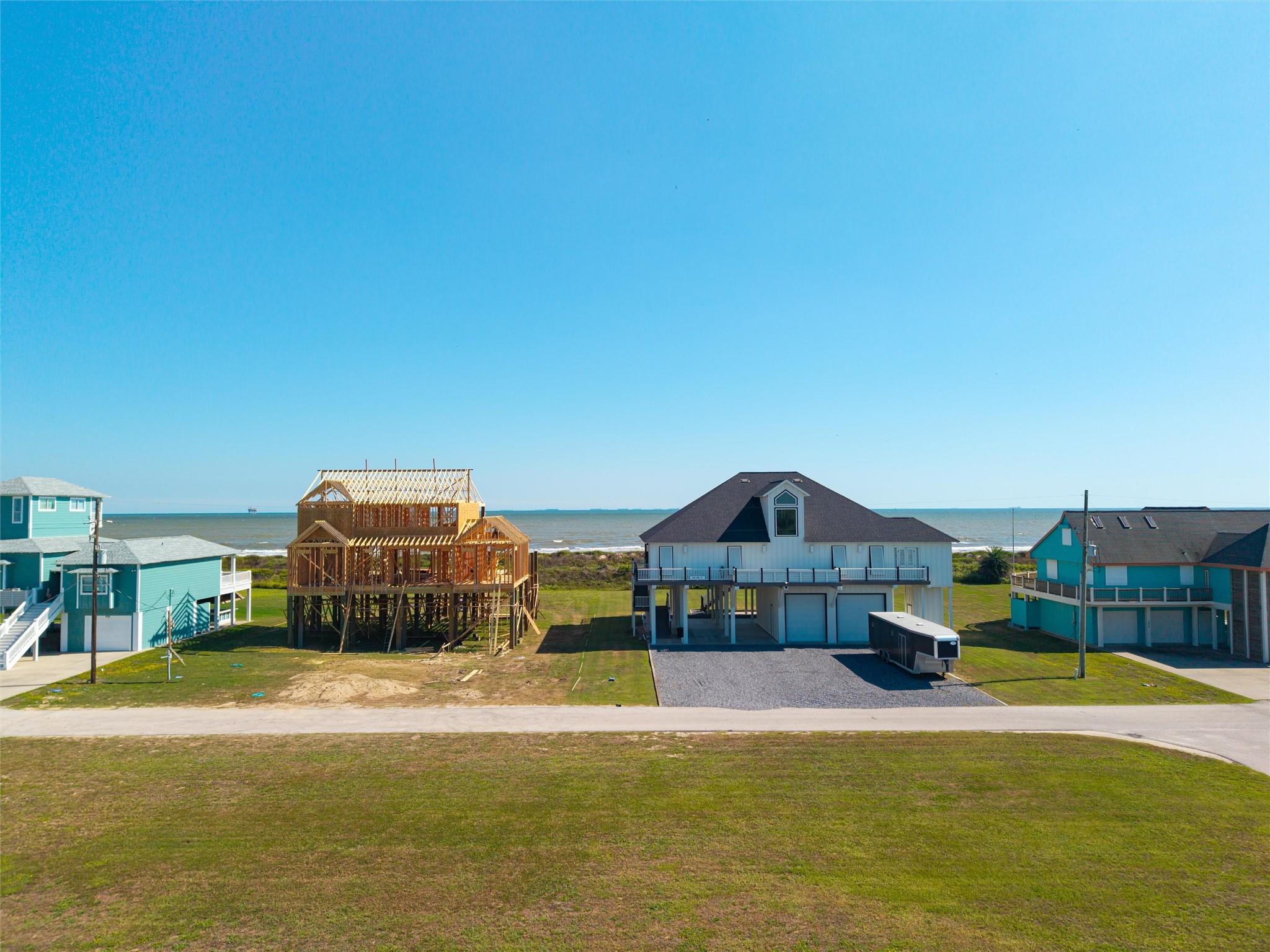 Beachfront homes beside the ocean, including a house under construction on raised supports.