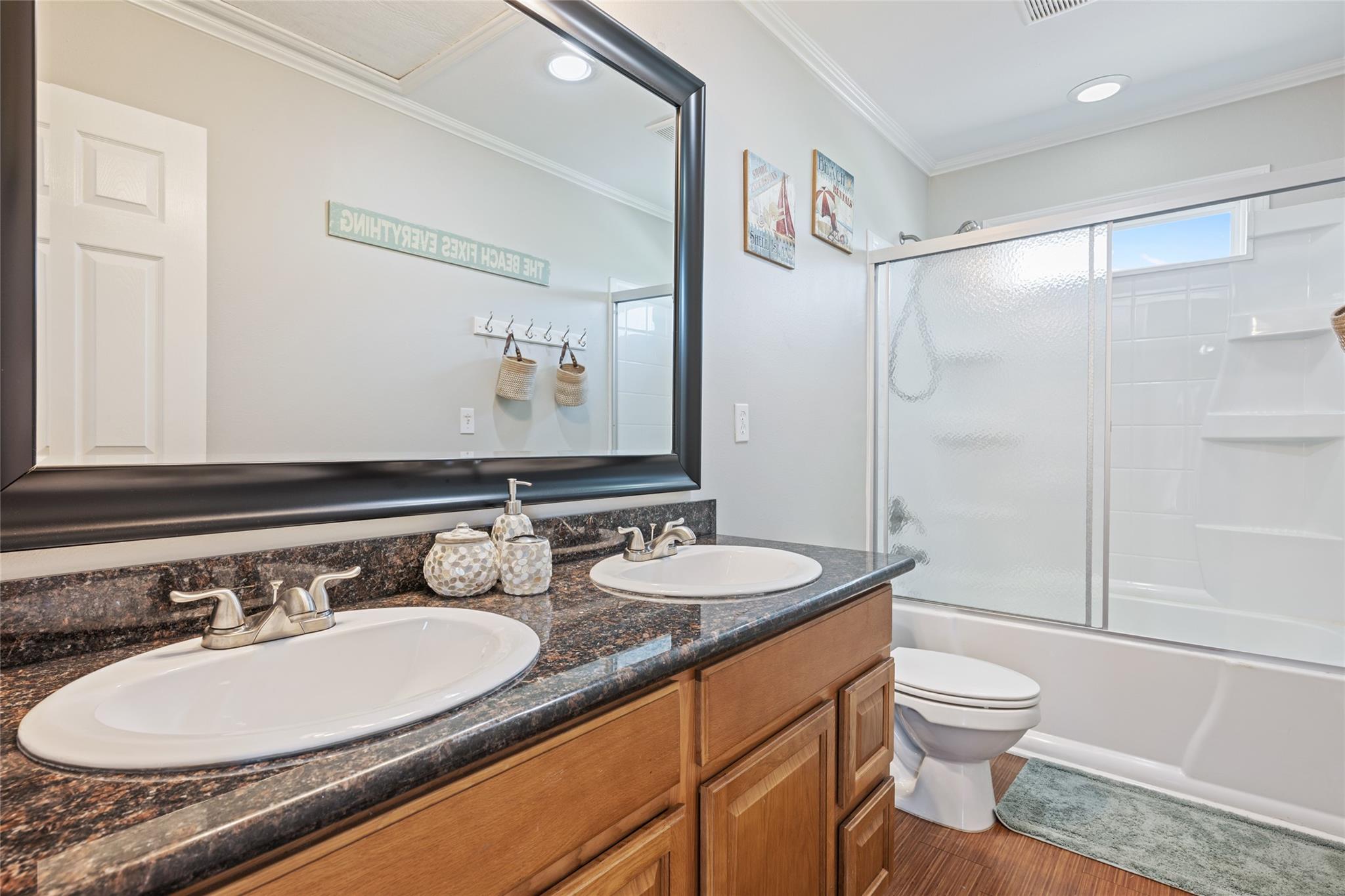 Bathroom with a double-sink granite vanity, wood cabinets, and a frosted-glass tub-shower.