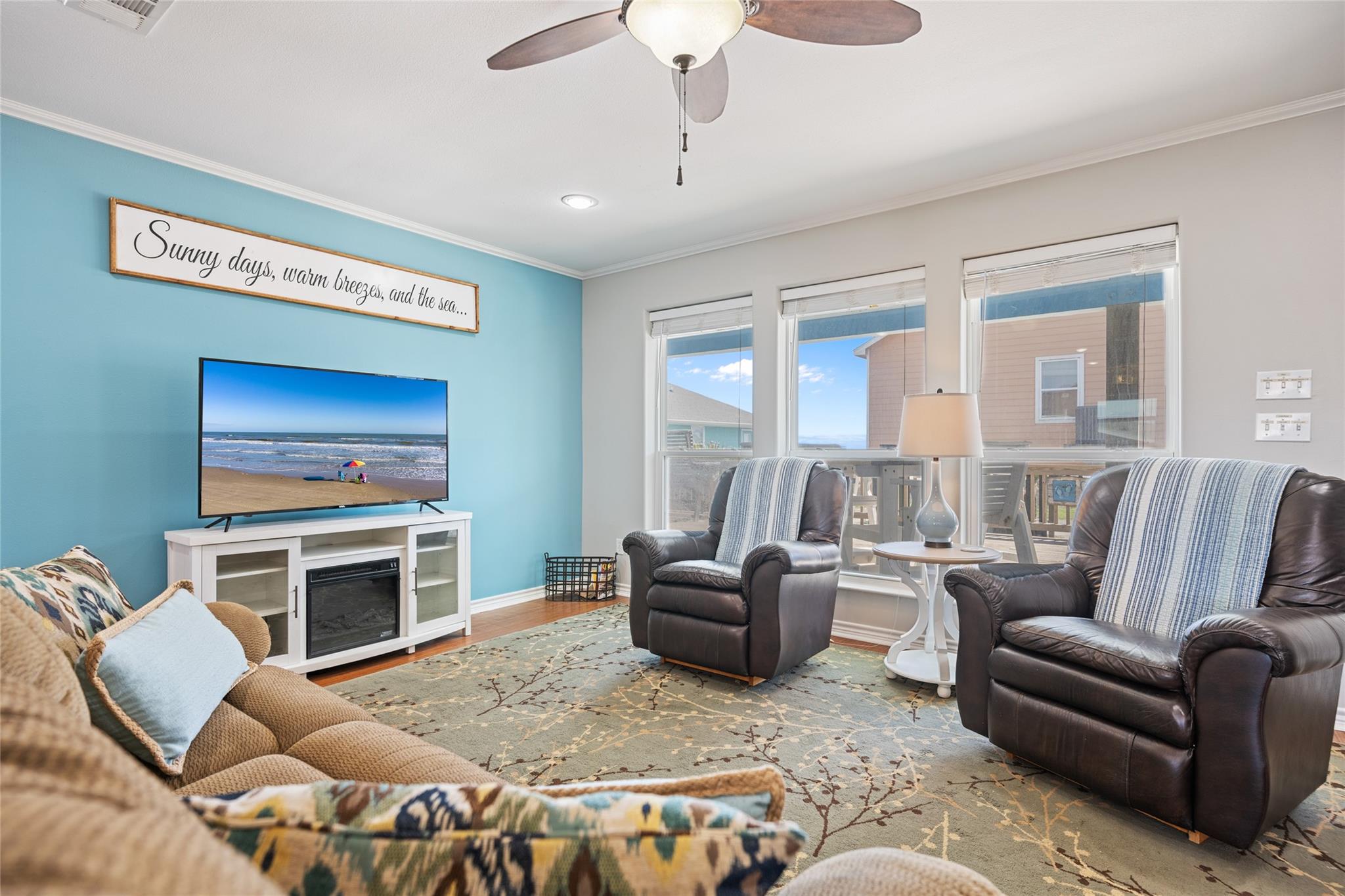 Furnished living room with a turquoise accent wall, leather recliners, and large windows overlooking a deck.