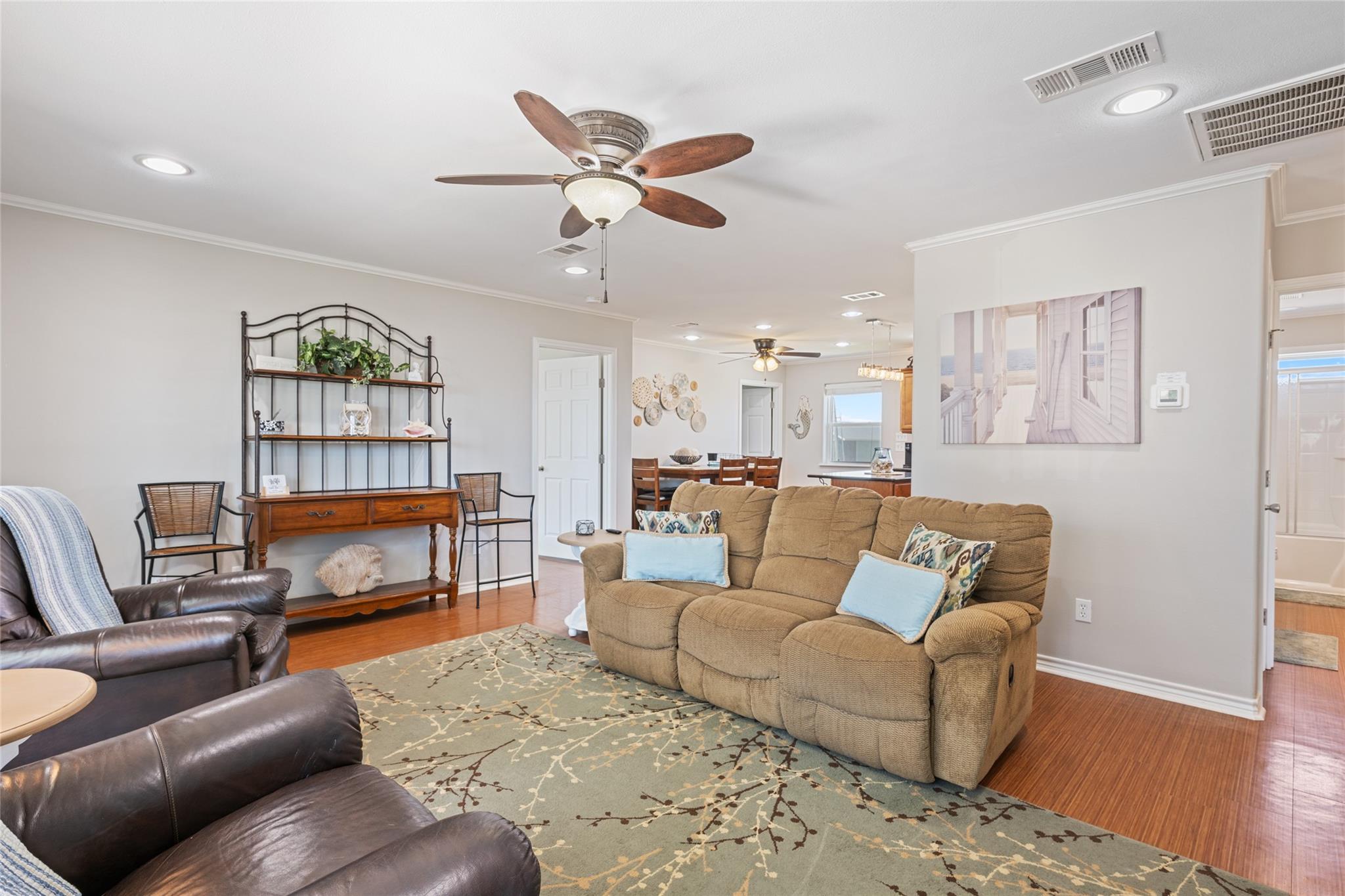 Furnished living room with tan reclining sofa, dark leather chairs, and an adjoining dining area.