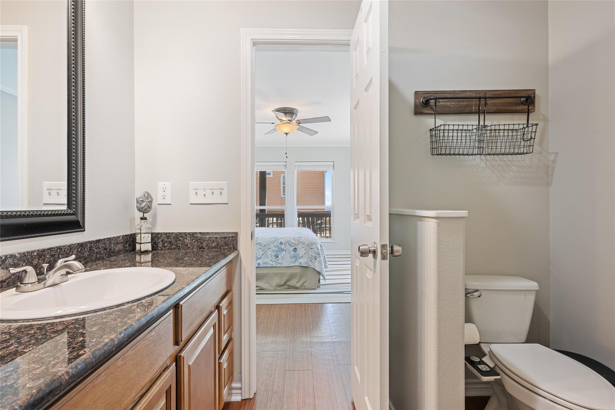 Bathroom with granite vanity and toilet, looking through an open doorway into a bedroom.