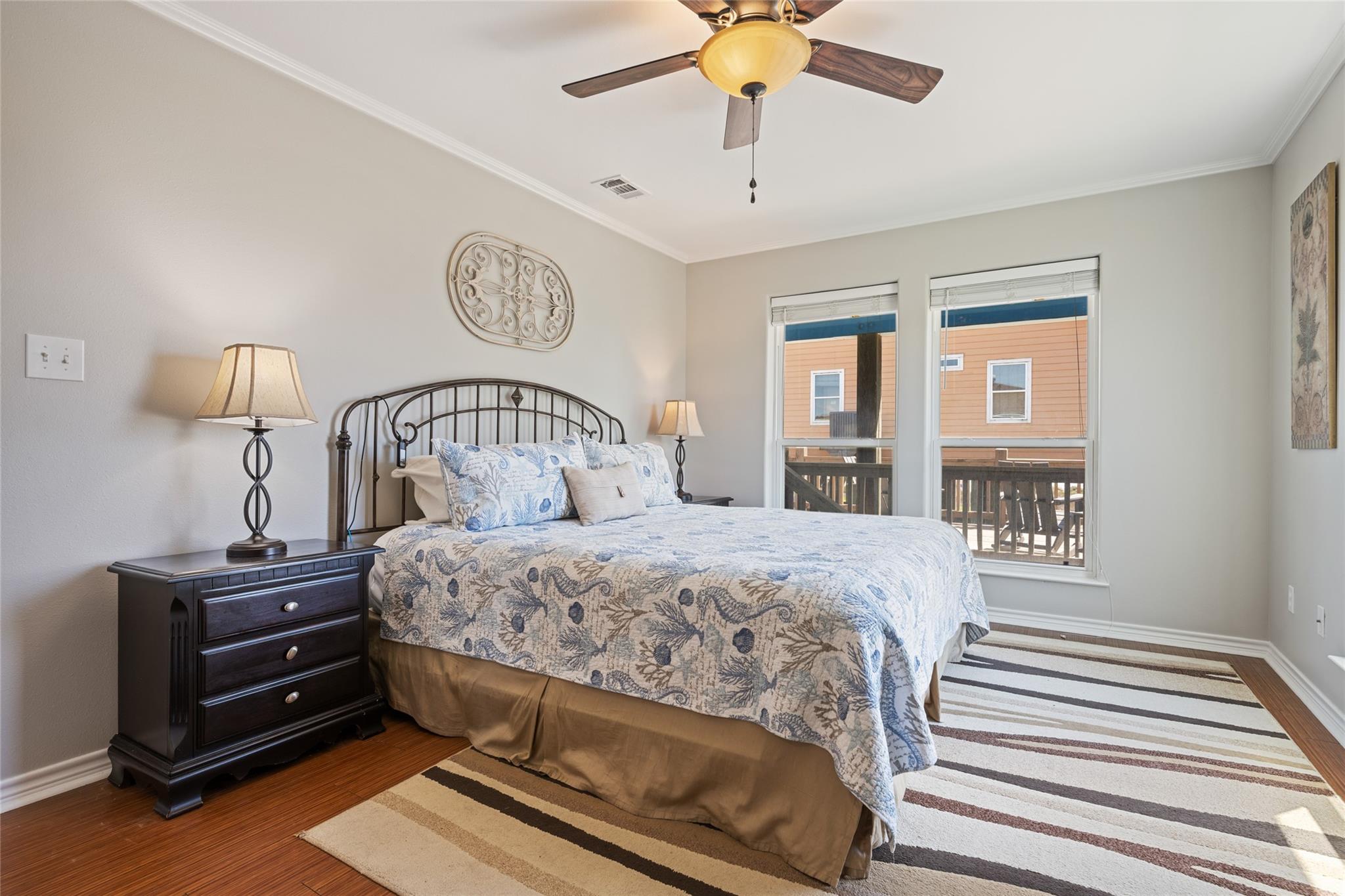 Bedroom with a blue-and-white patterned bedspread, dark wood nightstand, and two windows.