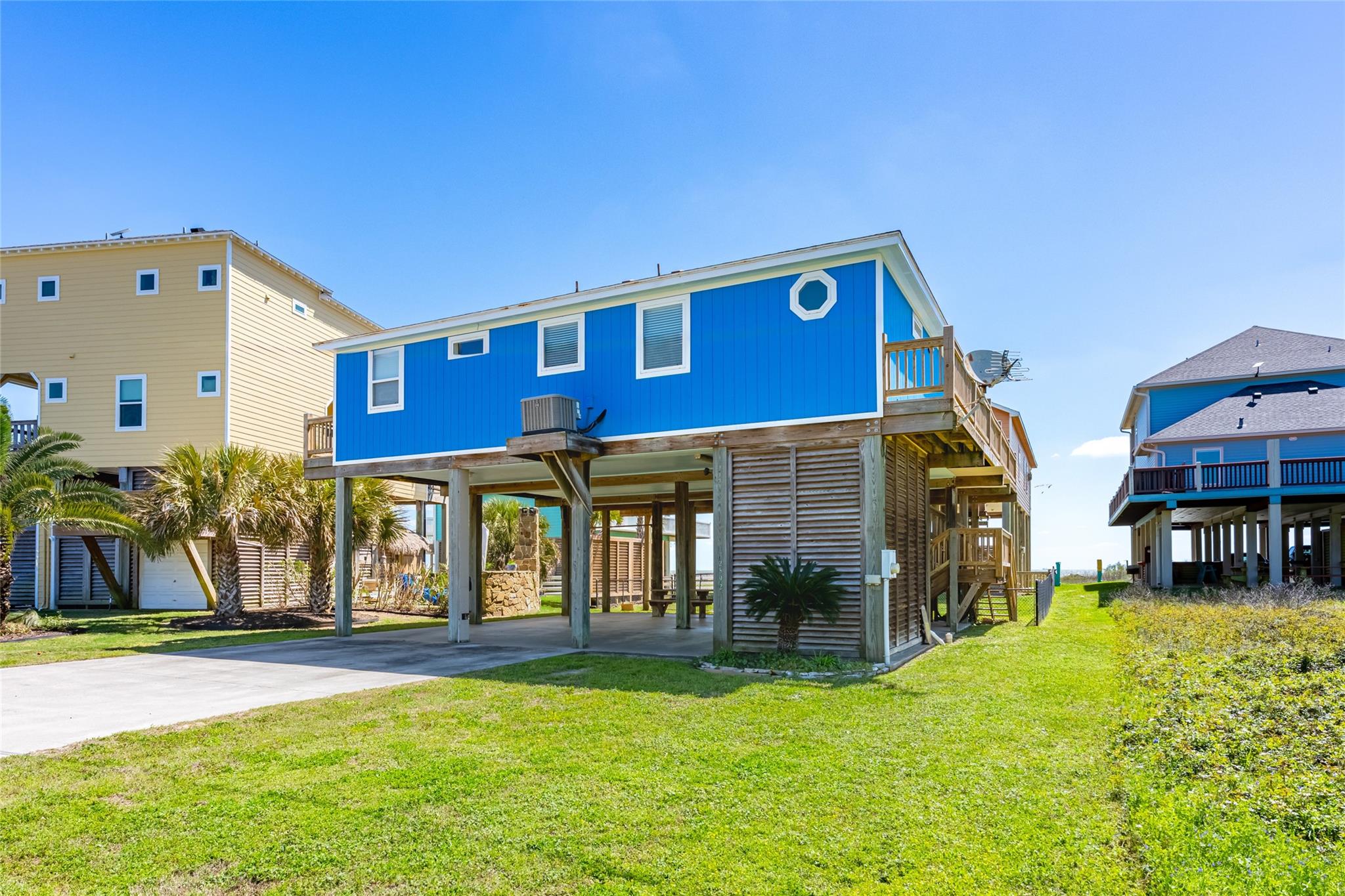 Blue elevated coastal house with an octagonal window, side deck, and covered parking beneath.