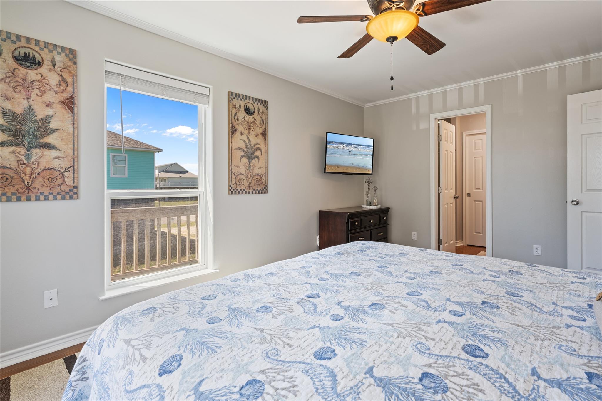 Bedroom with a shell-patterned quilt, ceiling fan, and window overlooking neighboring homes.