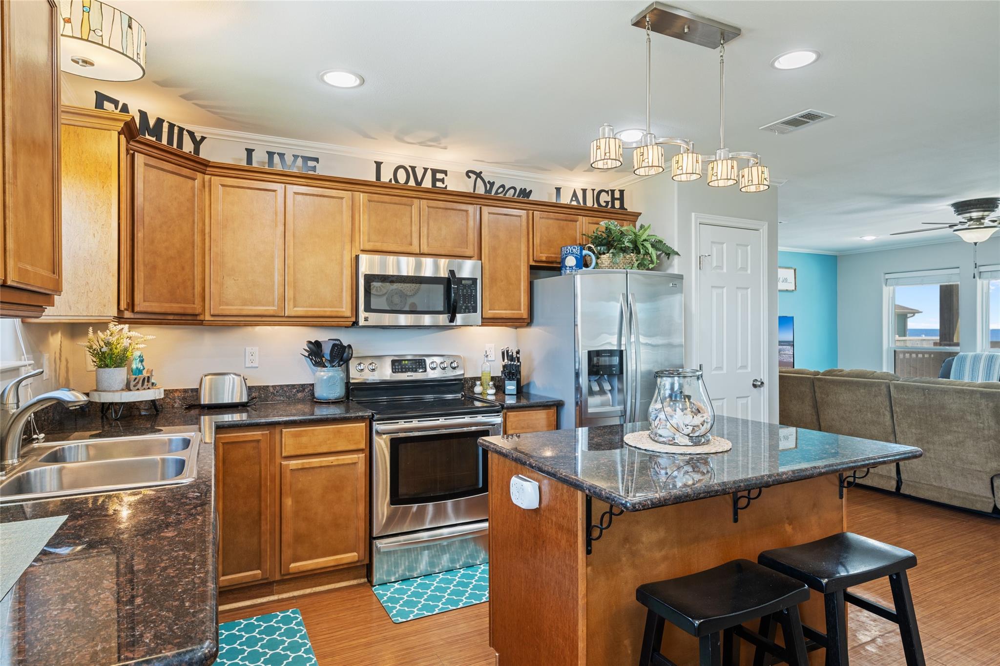 Kitchen with wood cabinets, granite counters, stainless appliances, and island bar beside the living room.
