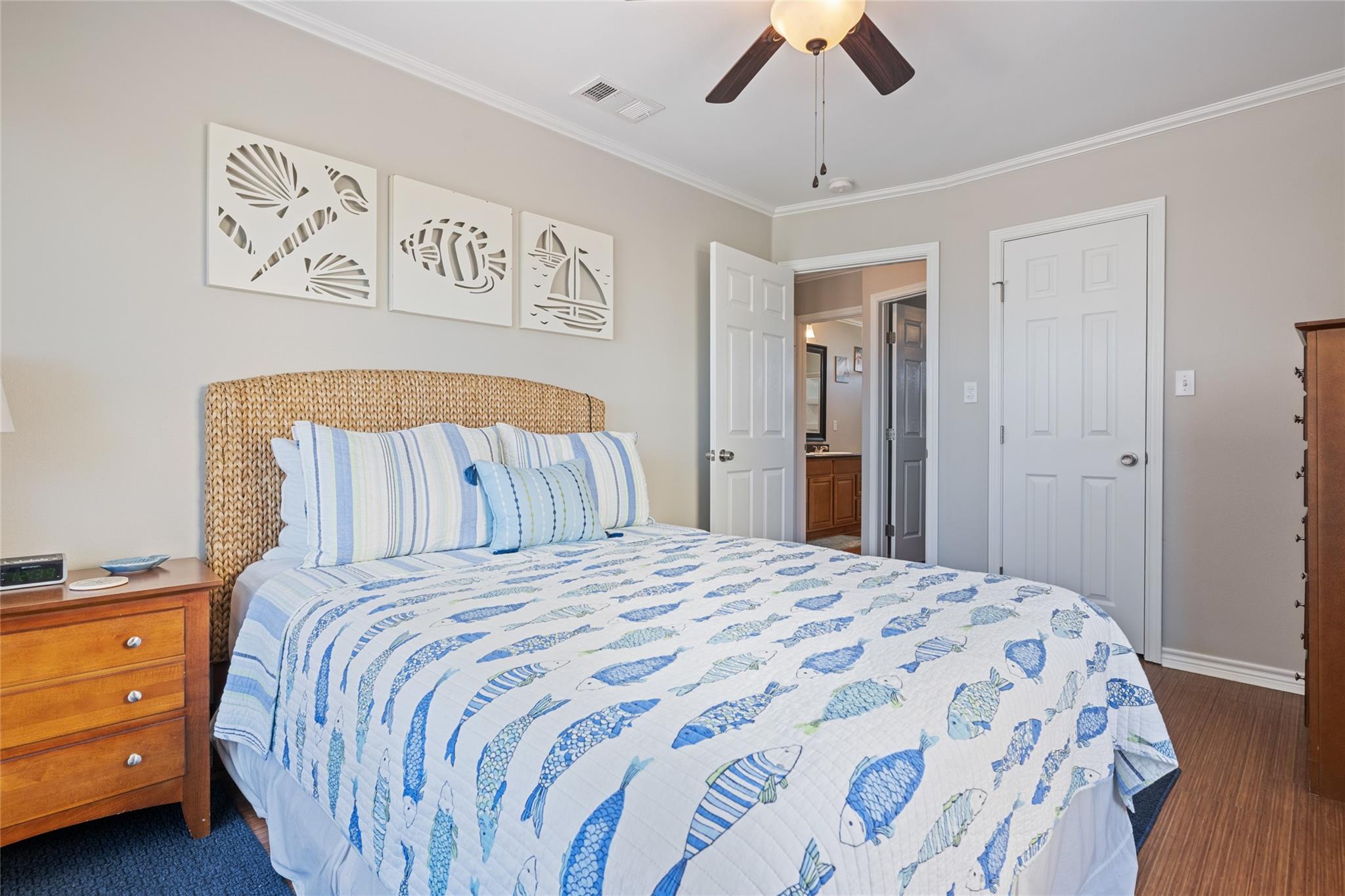 Bedroom with a woven headboard, blue fish-patterned bedding, and coastal wall art.