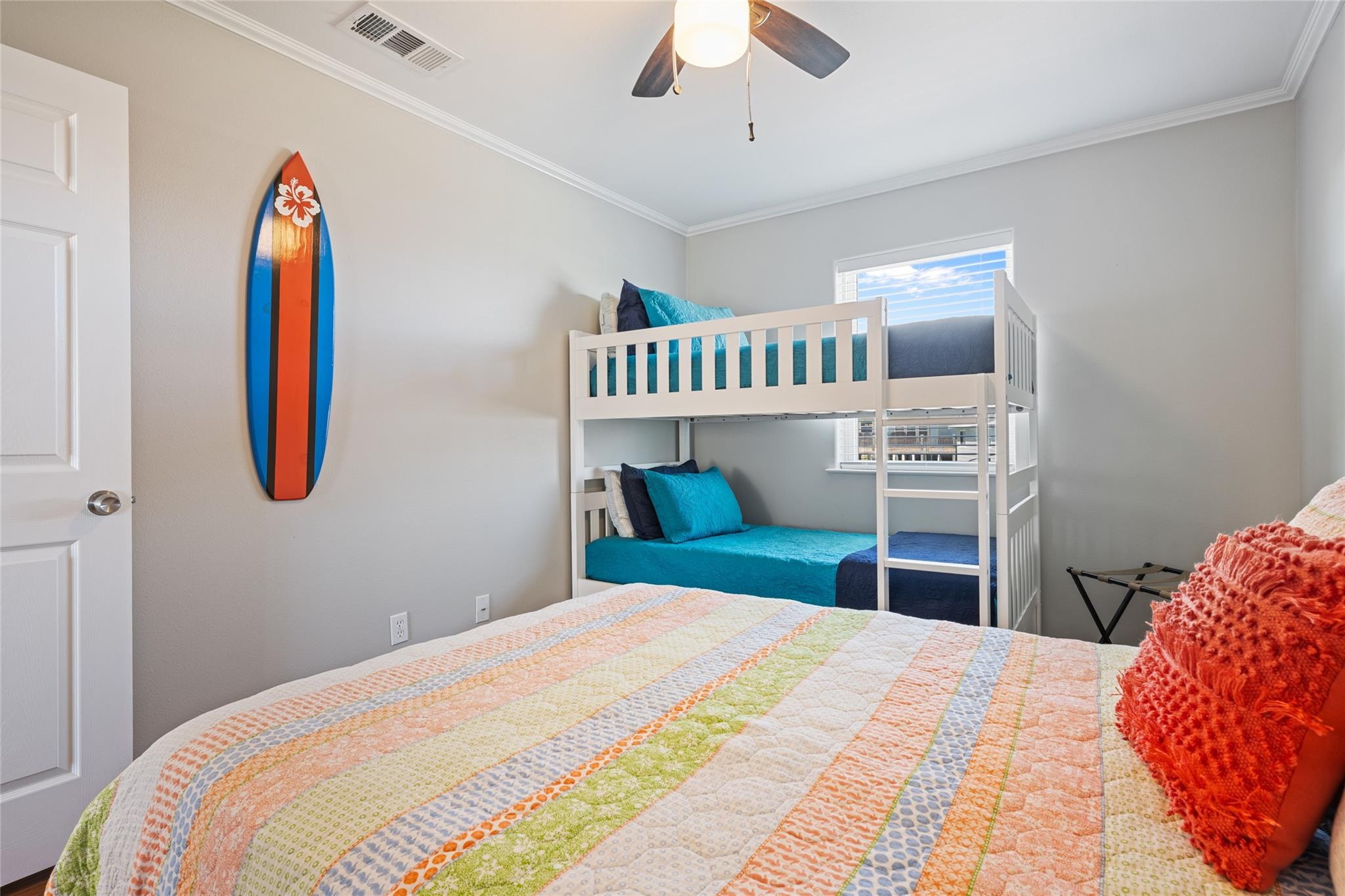 Bedroom with white bunk beds, turquoise bedding, and a colorful surfboard wall decoration.