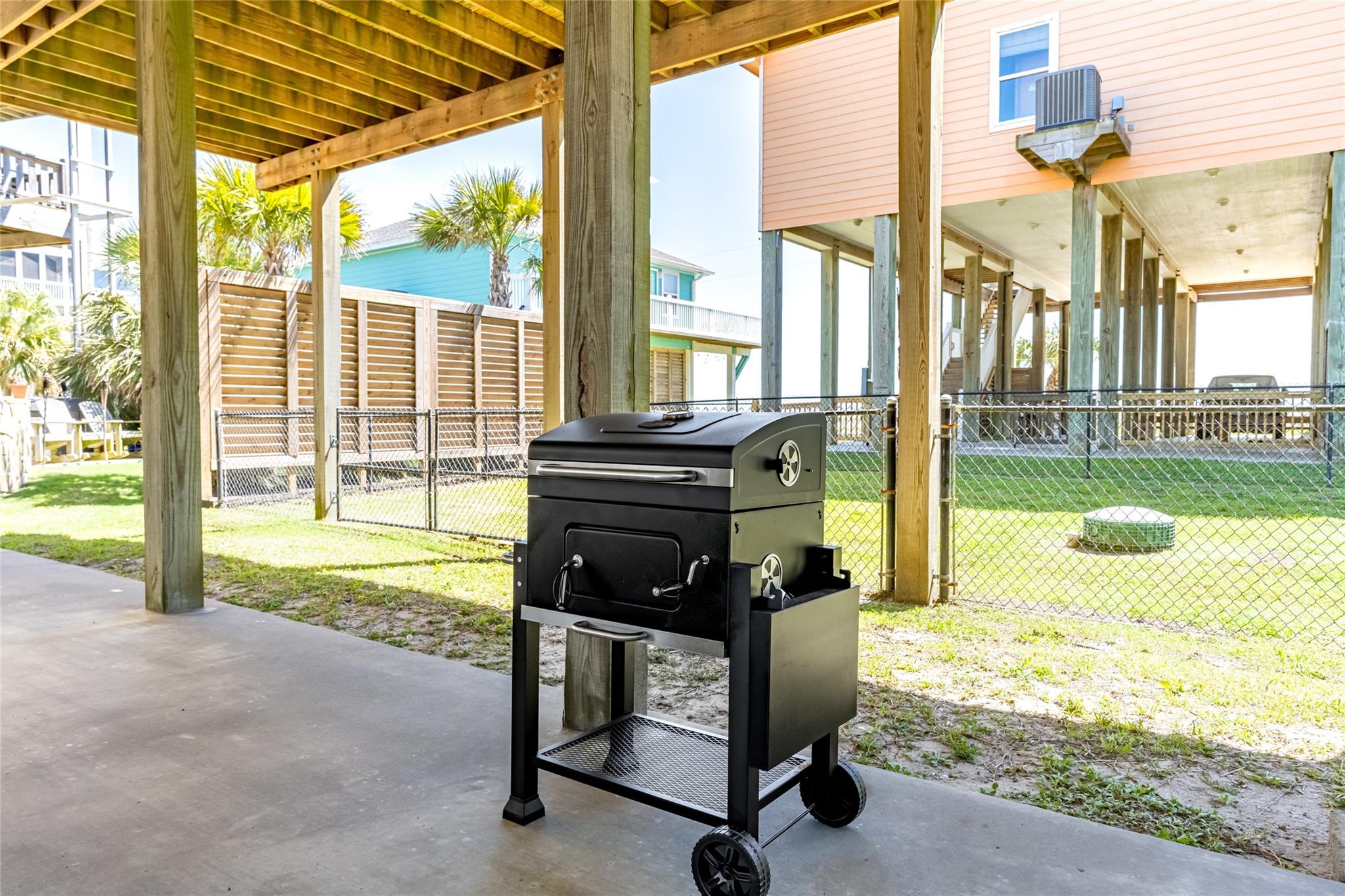 Covered patio with a black grill and fenced yard beneath a raised home.